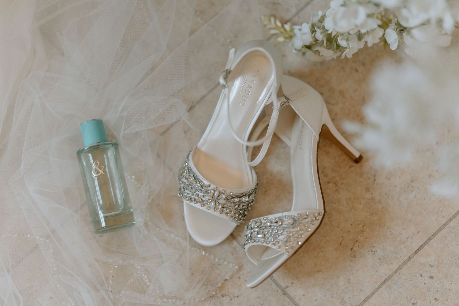 Sparkling bridal shoes and perfume bottle arranged on white fabric at Bourton Hall.