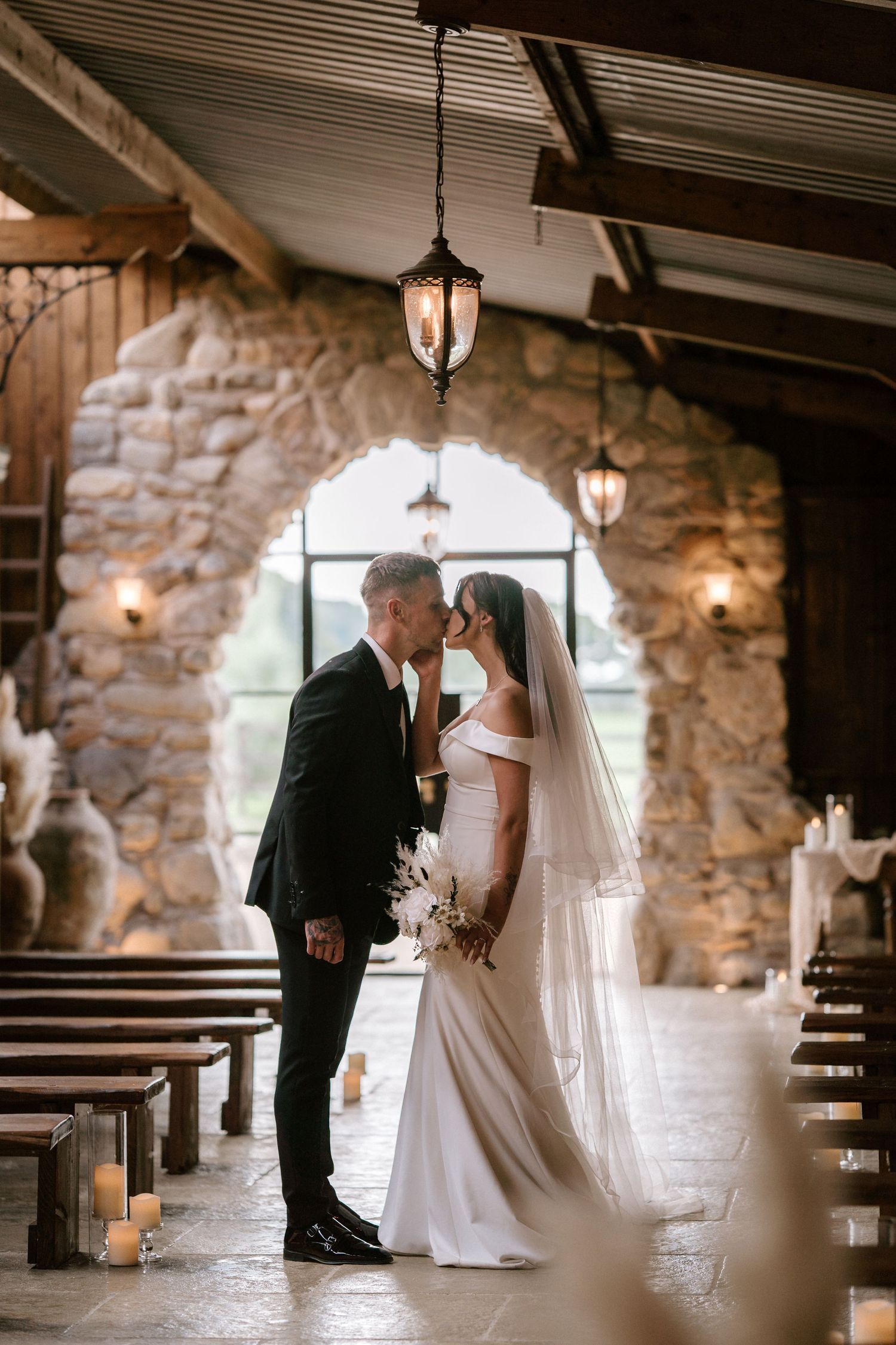 Romantic wedding portrait in stone archway with hanging lanterns creating intimate ambiance.