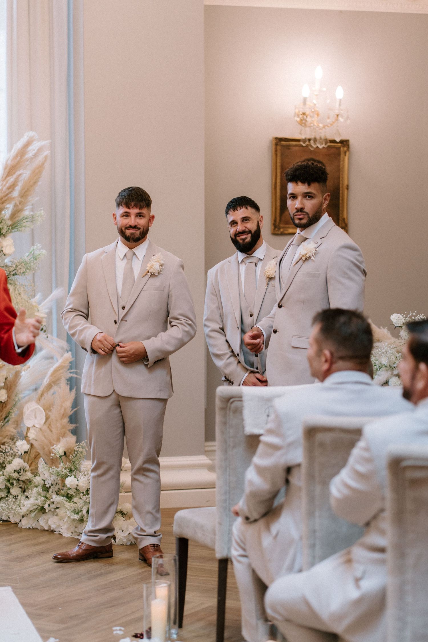 Groomsmen in light gray suits share a playful moment before the wedding ceremony in an elegant room.