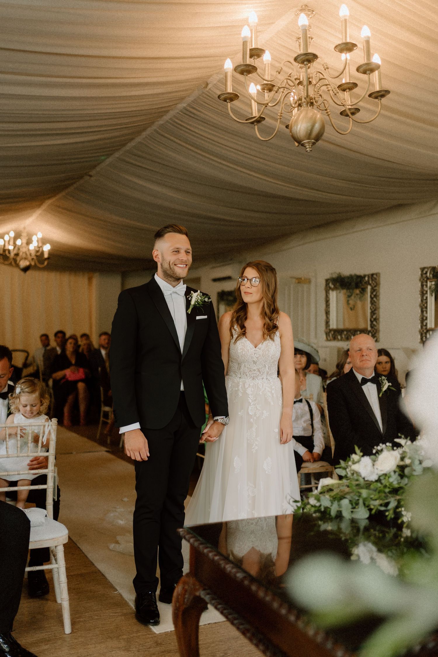 Couple walking together during indoor wedding reception under draped fabric ceiling with elegant chandeliers at Warwick House.