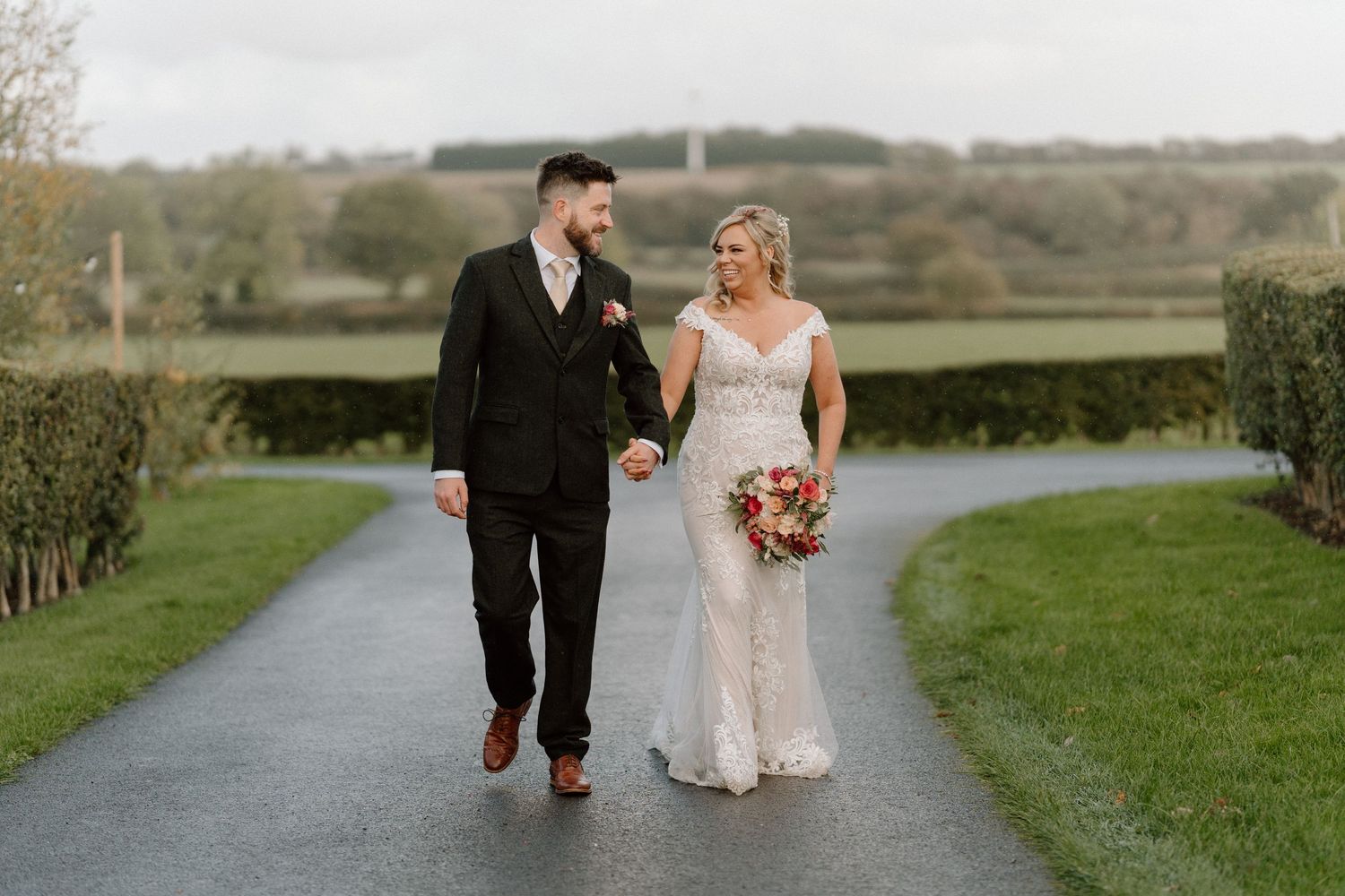 Newlyweds walking together on a garden path surrounded by lush greenery at The Old Cow Shed.