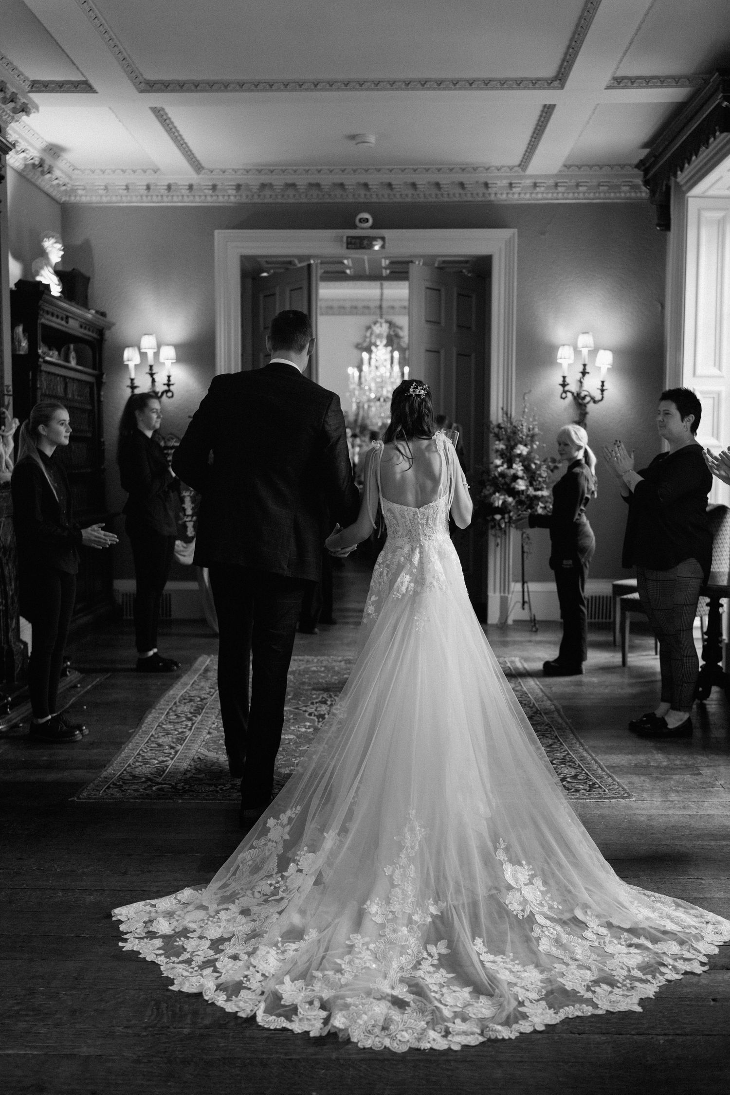 Elegant black and white wedding ceremony photo showing the bride's lace gown train in a chandelier-lit room at Prestwold Hall.