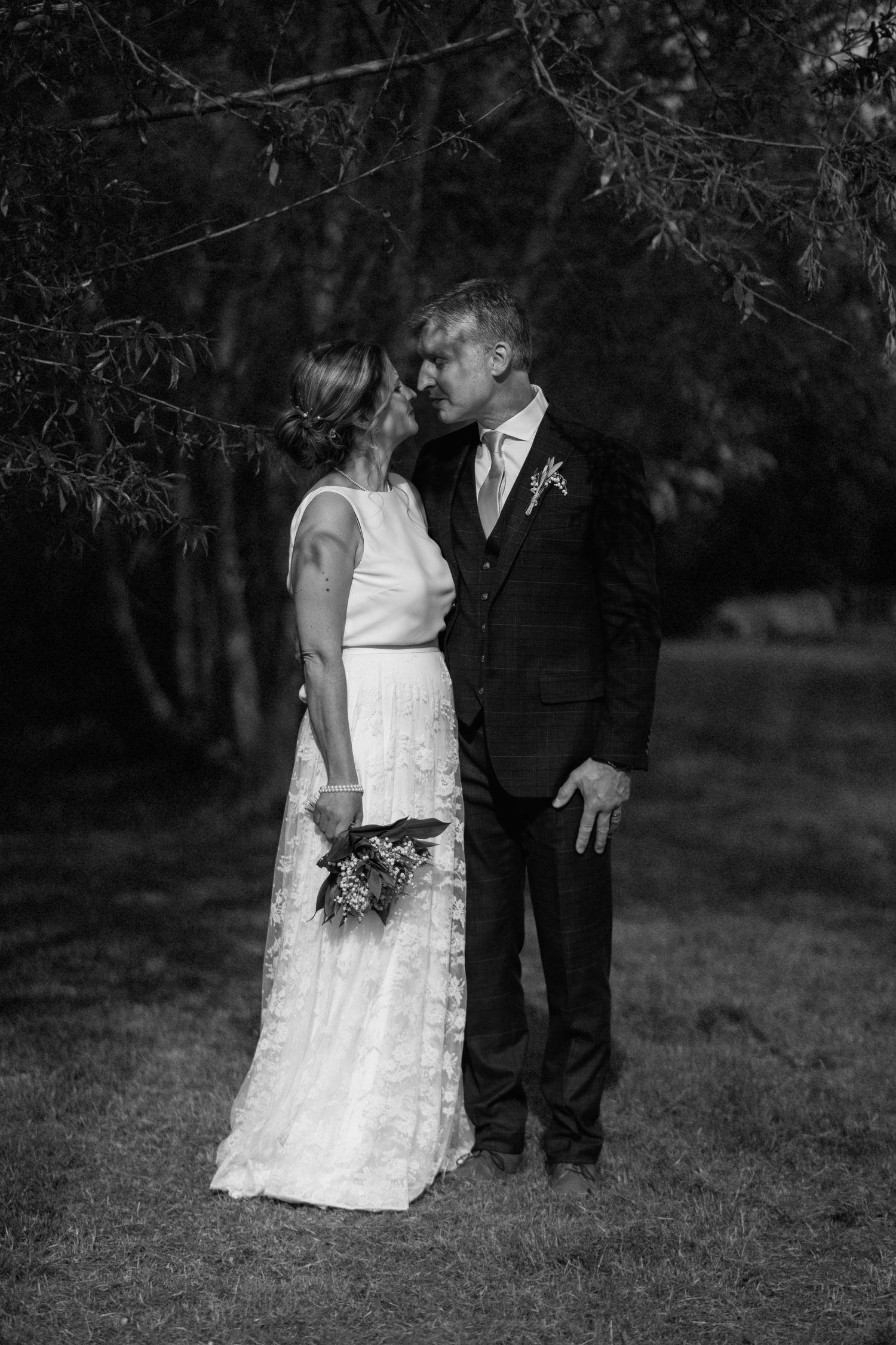 A timeless black and white wedding photo capturing a romantic moment between newlyweds under tree branches at Swallows Nest Barn.