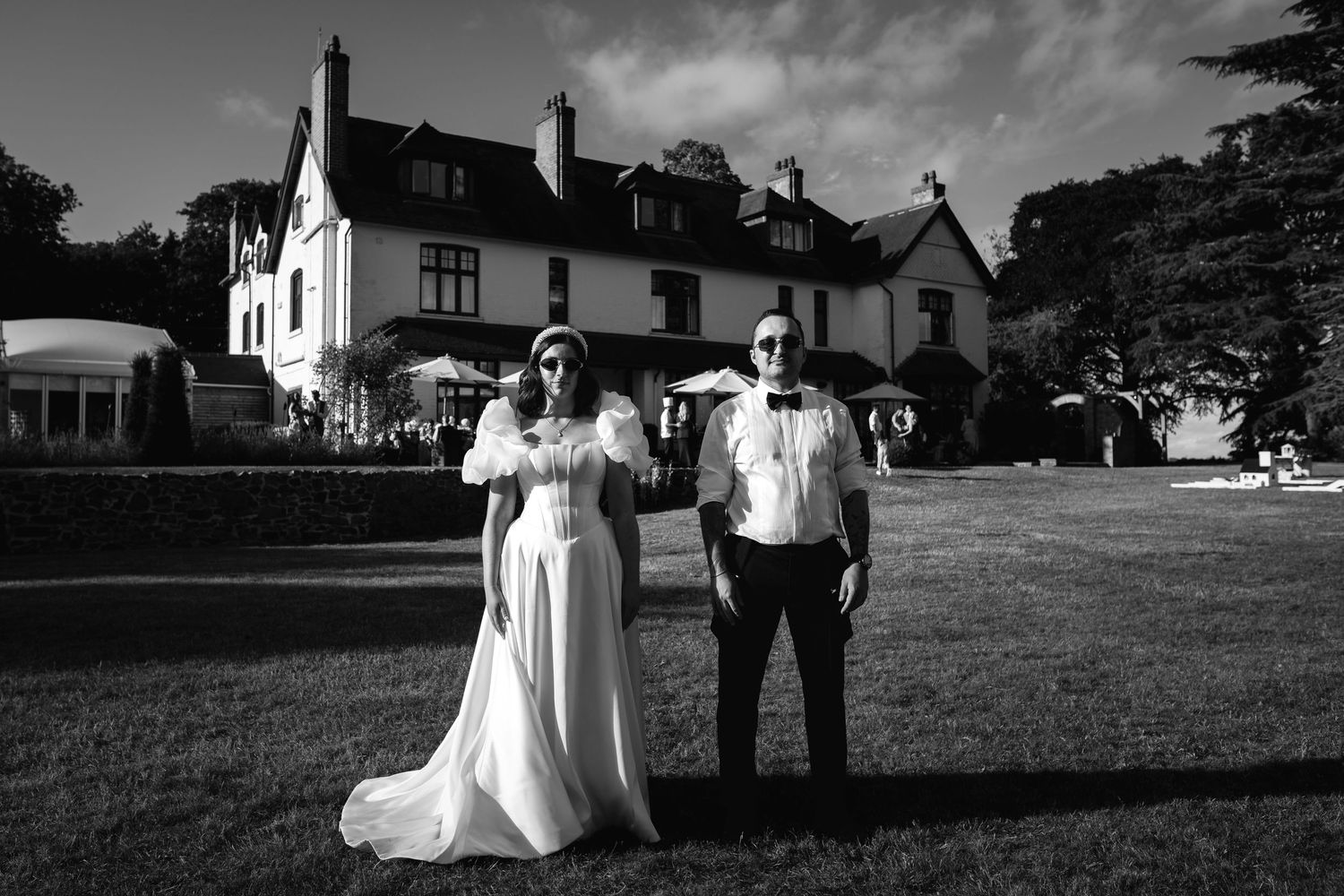 Black and white photo of a bride and groom posing outside an elegant country house venue.