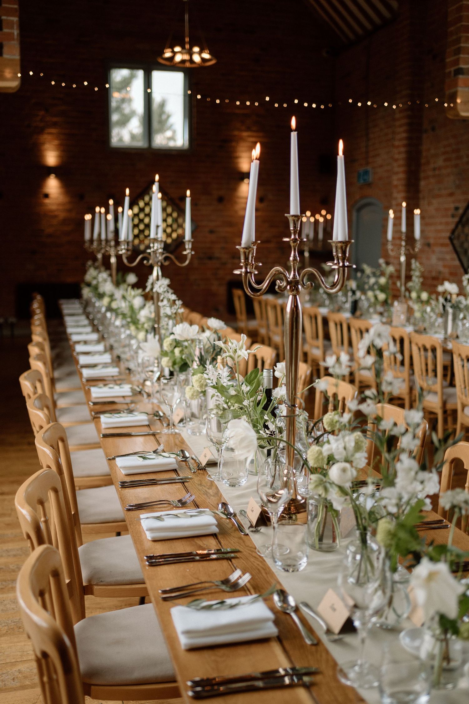 Elegant rustic wedding reception table with white candelabras, floral arrangements and wooden chairs at Swallows Nest Barn.