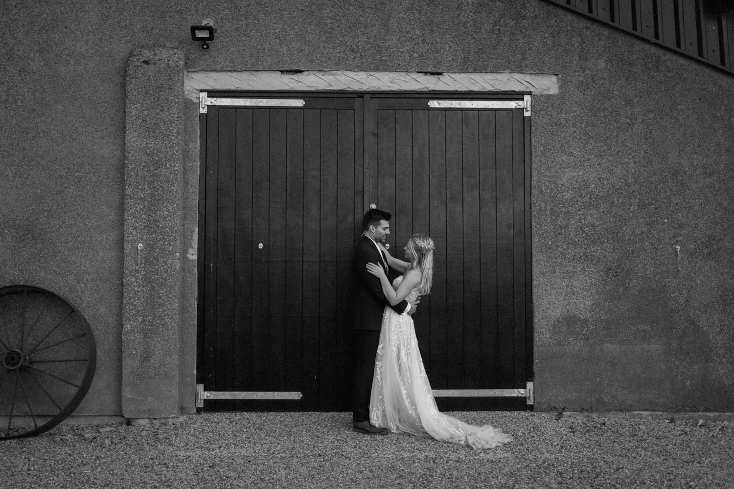 A black and white wedding photograph of a couple embracing in front of rustic wooden barn doors at Milling Barn.