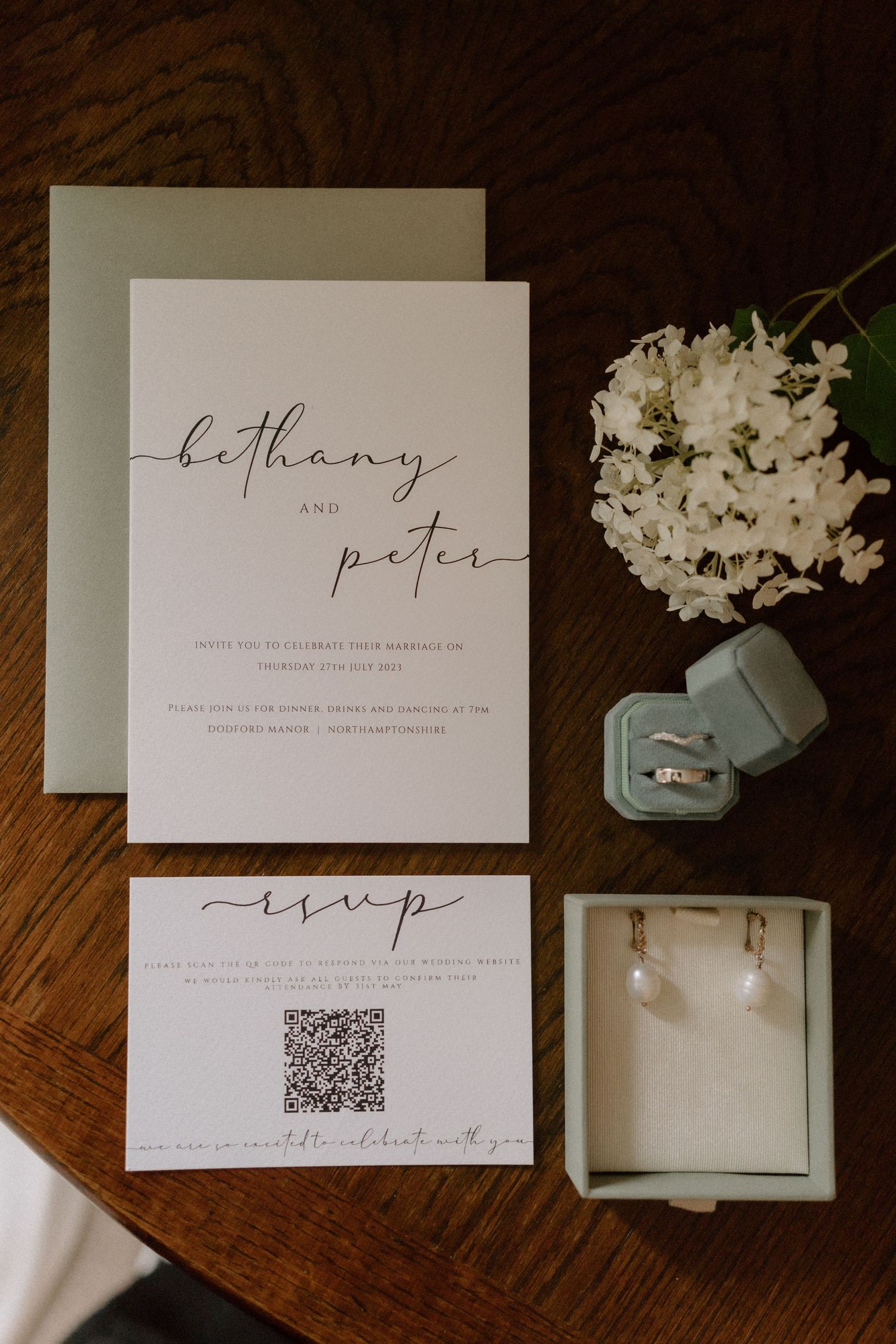 Wedding invitation suite with calligraphy, ring box, and white hydrangea on wooden surface at Dodford Manor.