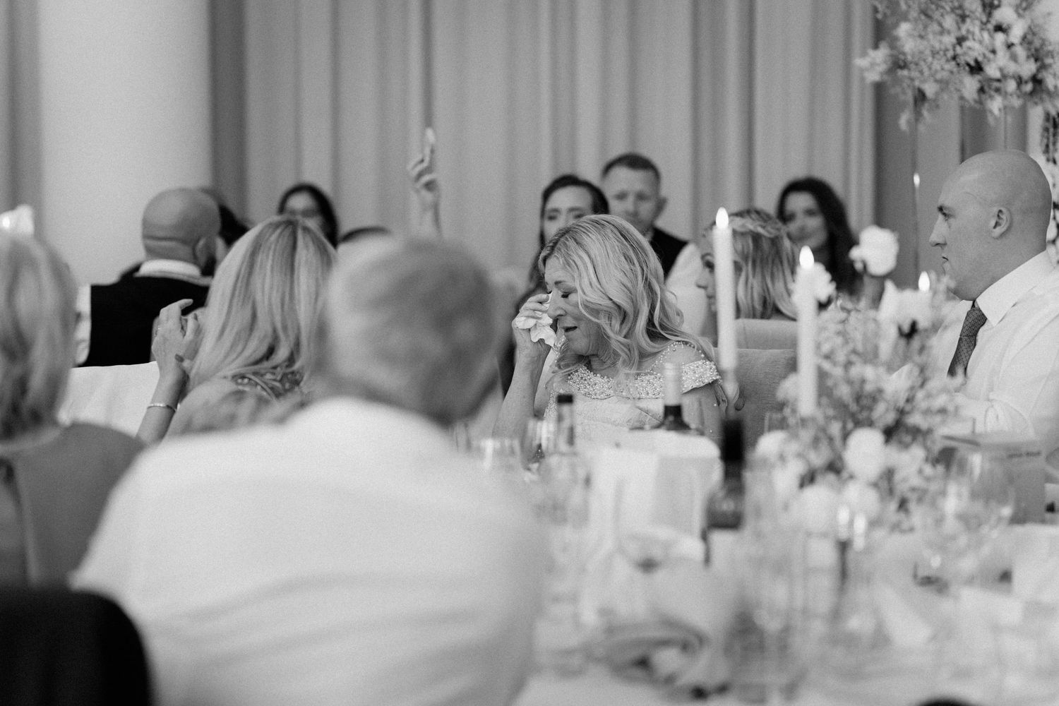 Wedding reception guests gathered around elegant tables with floral centerpieces.