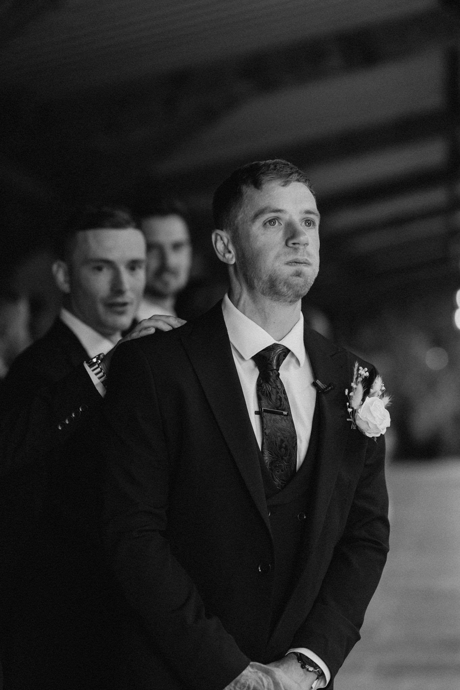 Black and white photo of an elegant groom and groomsmen in formal attire at an indoor venue.