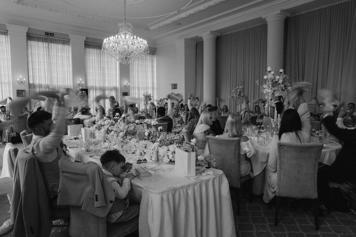 Panoramic view of an elegant wedding reception ballroom with crystal chandeliers and table settings.