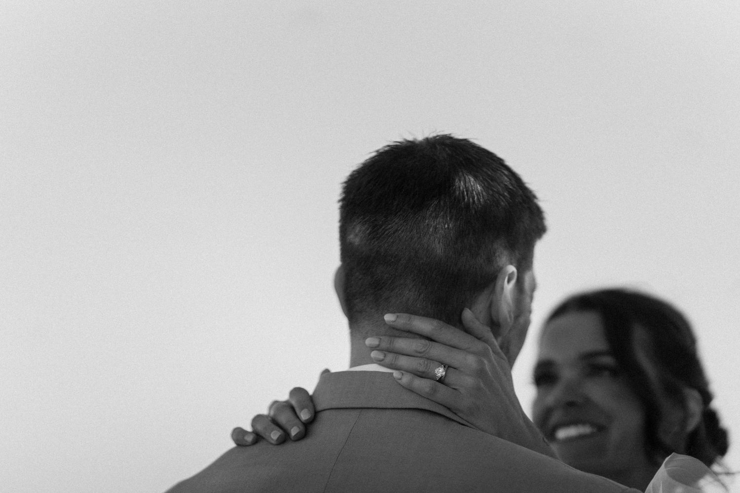 Black and white photo of a couple sharing a tender dance, bride smiling as groom holds her close at their wedding.