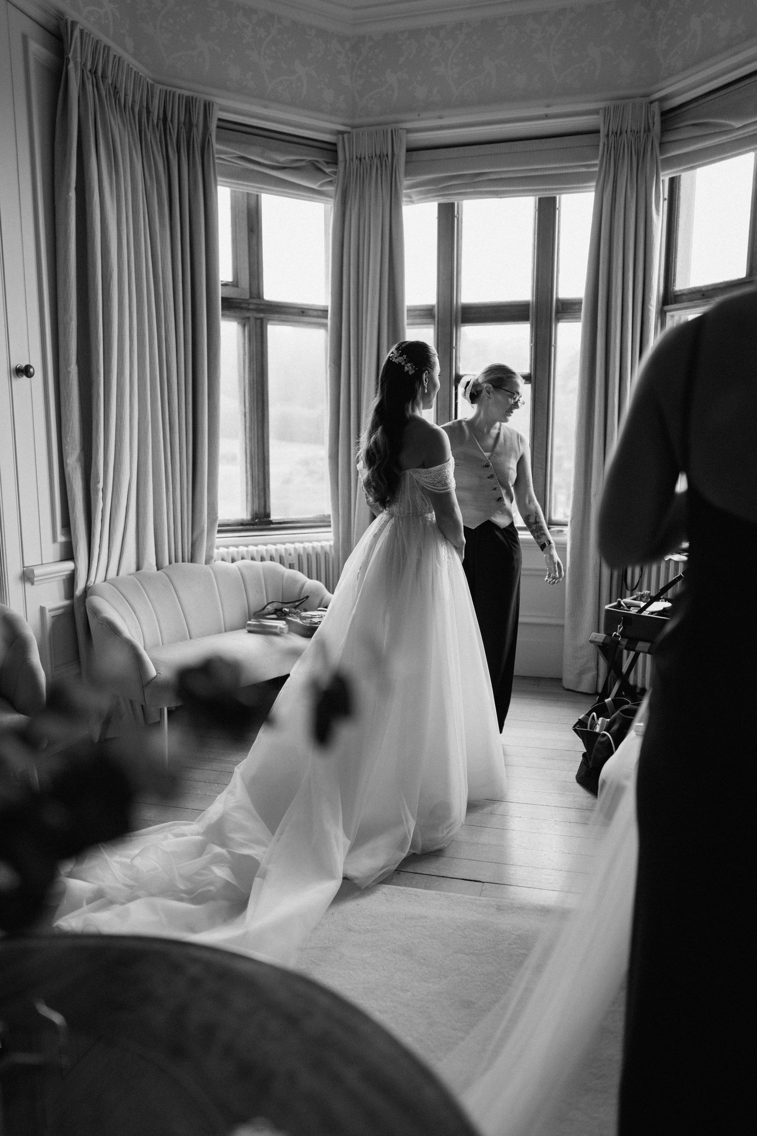 A black and white wedding preparation scene by large windows in an elegant room at Harlaxton Manor.