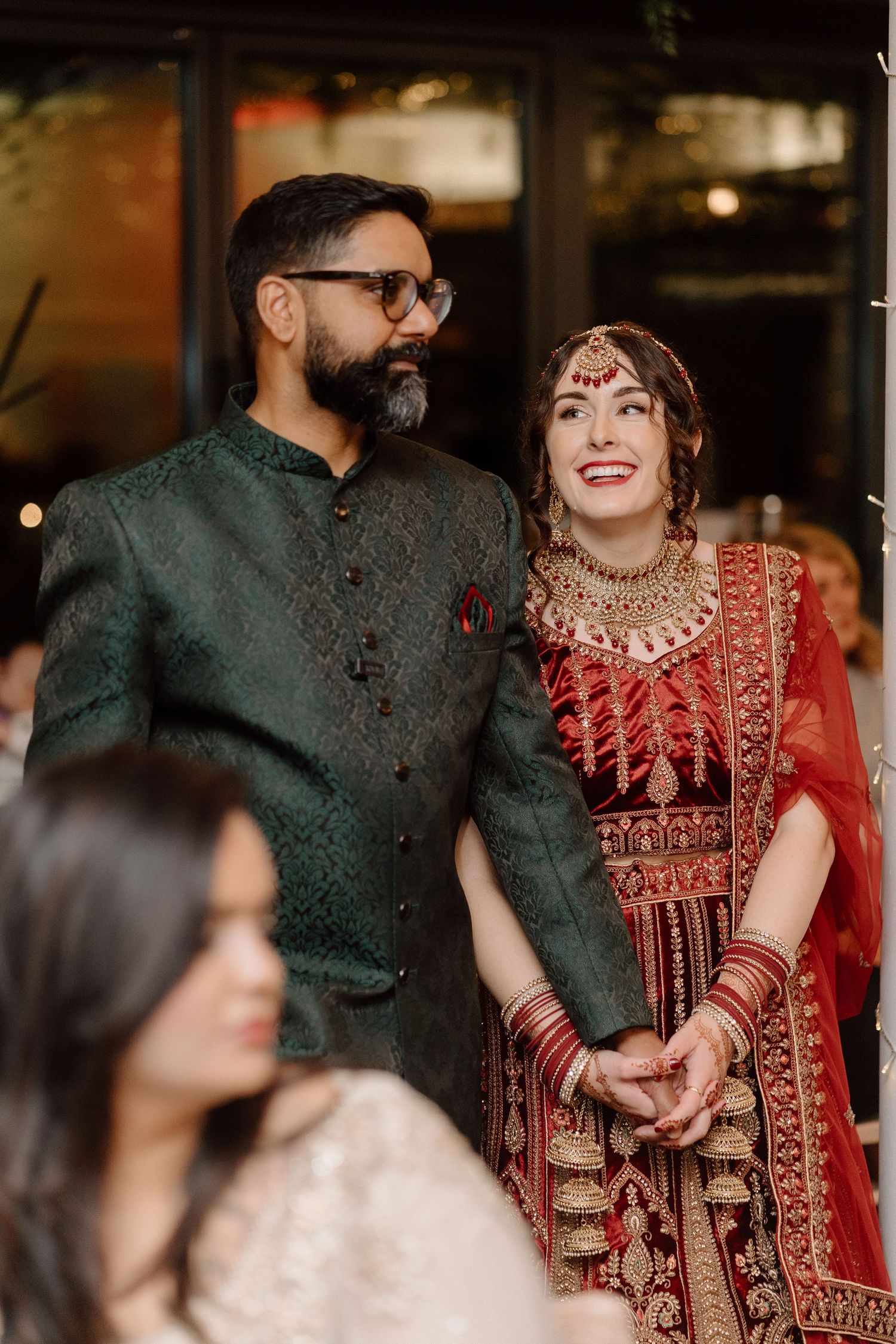 A couple in traditional South Asian wedding attire smiling during their celebration at The Glasshouse in Leamington Spa.