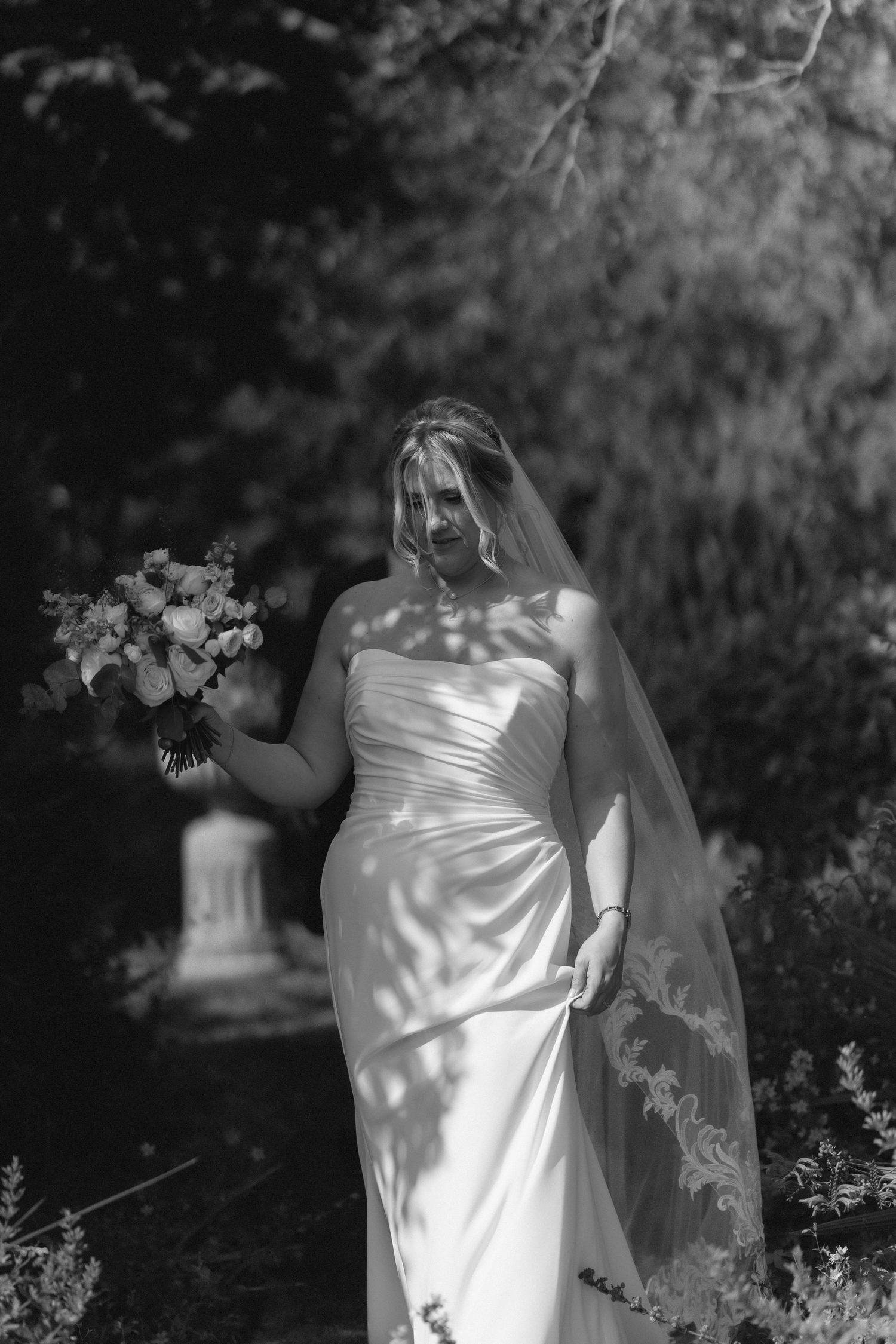 A wedding dress glows in dappled sunlight while a bouquet of flowers completes the ethereal garden scene at Nuthurst Grange.