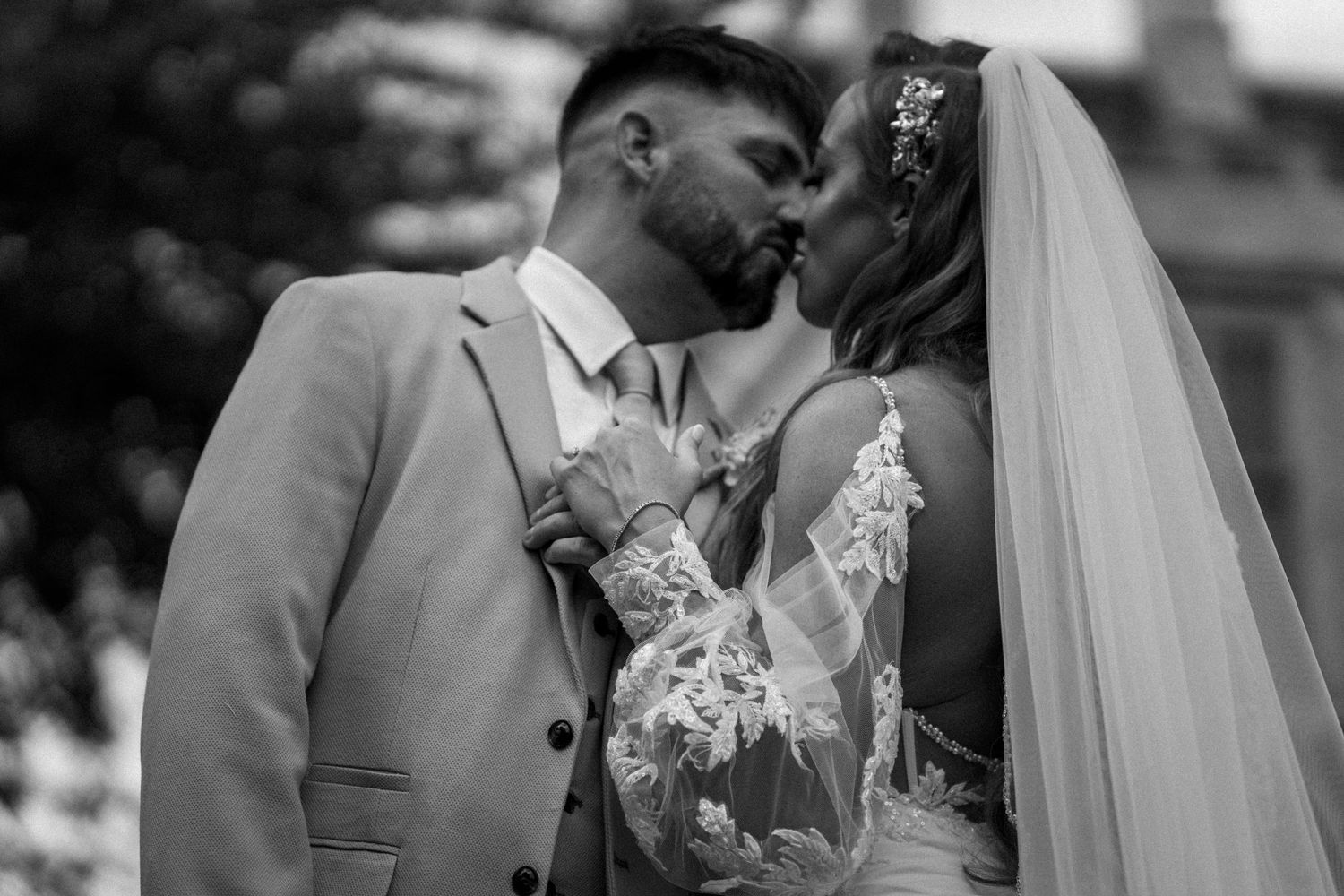 A tender moment shared between newlyweds in black and white, with bride in lace dress and groom in light suit.