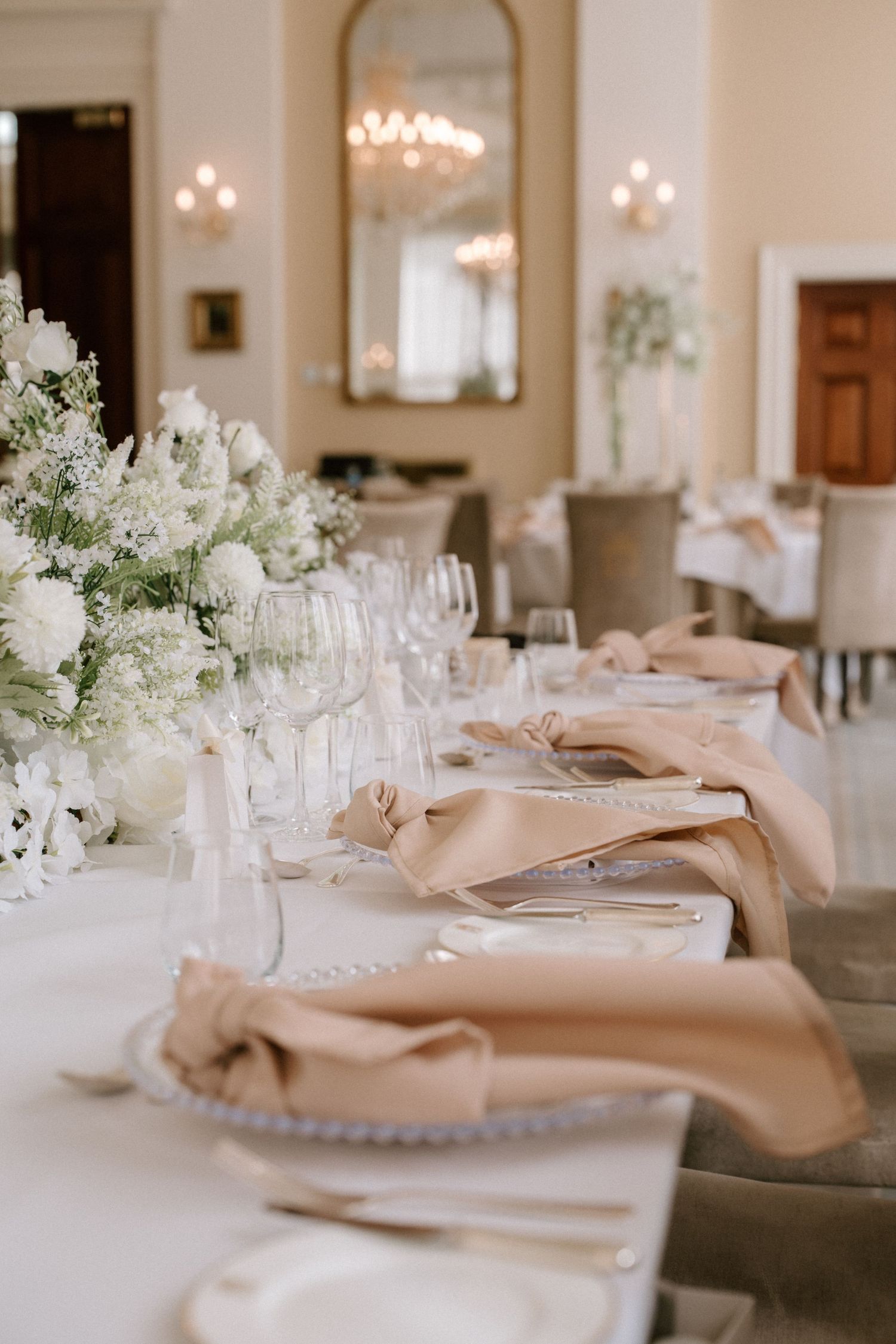 Elegant table setting with white floral centerpieces and beige napkins at a wedding reception.