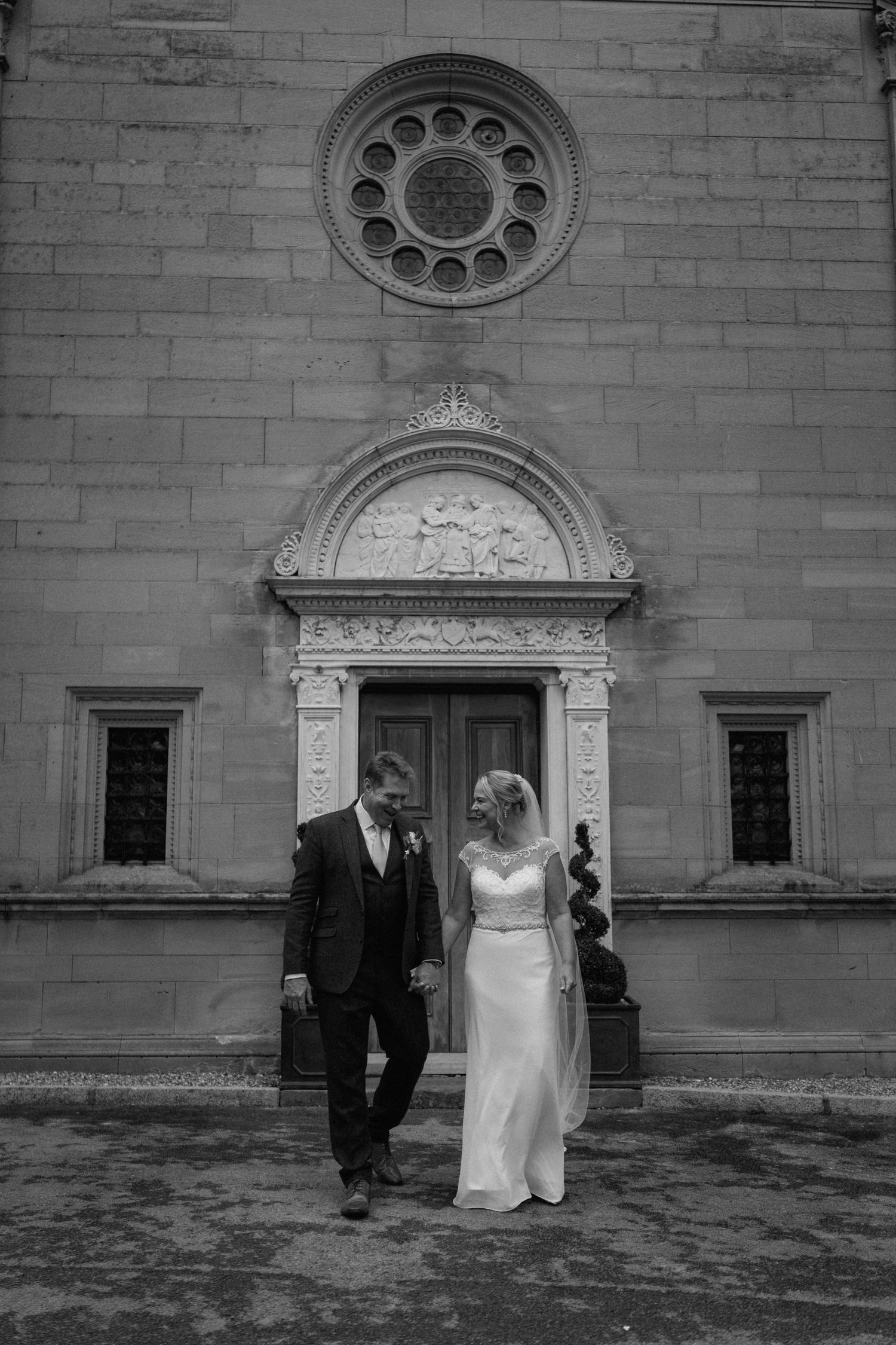 Architectural wedding portrait in front of stone building with ornate circular window at Bourton Hall.