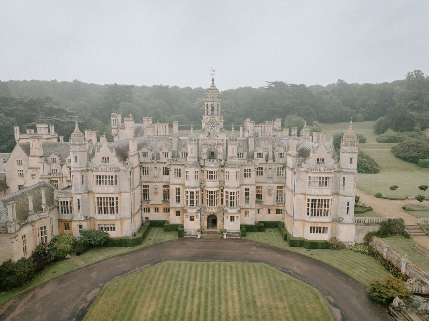 Aerial view of a magnificent Gothic Revival mansion with manicured grounds in foggy weather at Harlaxton Manor.