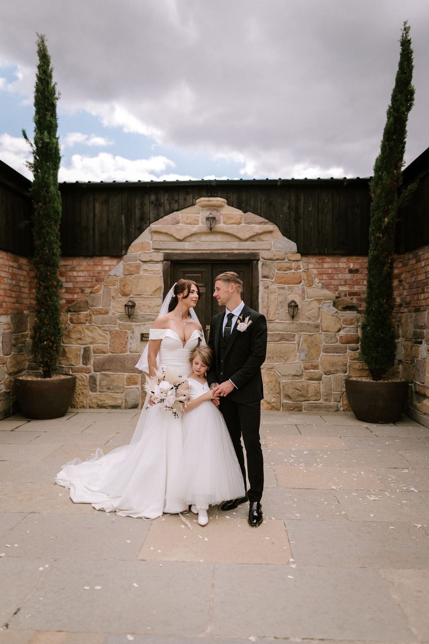 Stone archway framed by cypress trees creates beautiful wedding portrait setting.