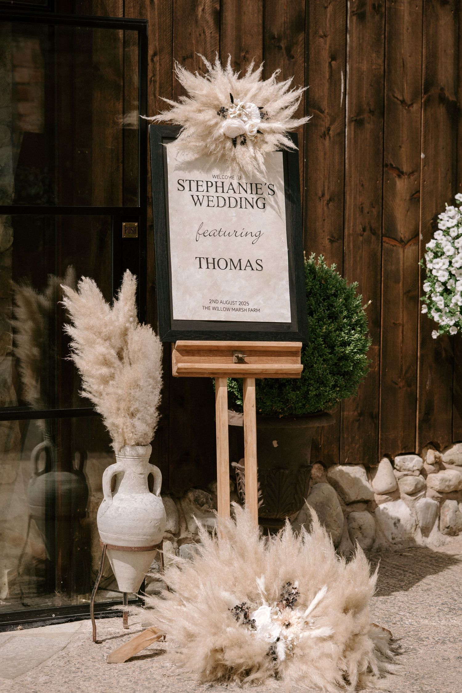 A rustic wedding welcome sign for Stephanie and Thomas decorated with pampas grass and displayed on a wooden easel.