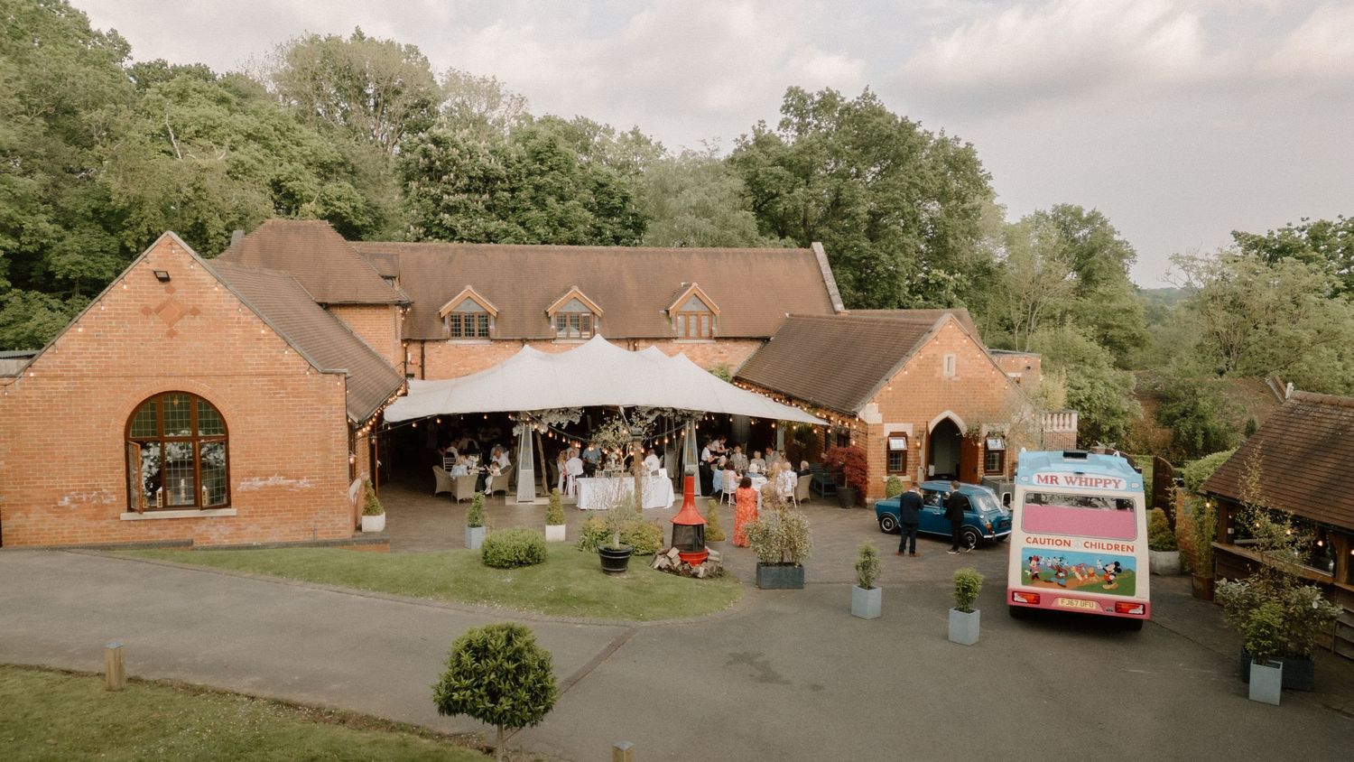 Brick wedding venue with curved entrance and parking area surrounded by trees at Nuthurst Grange.