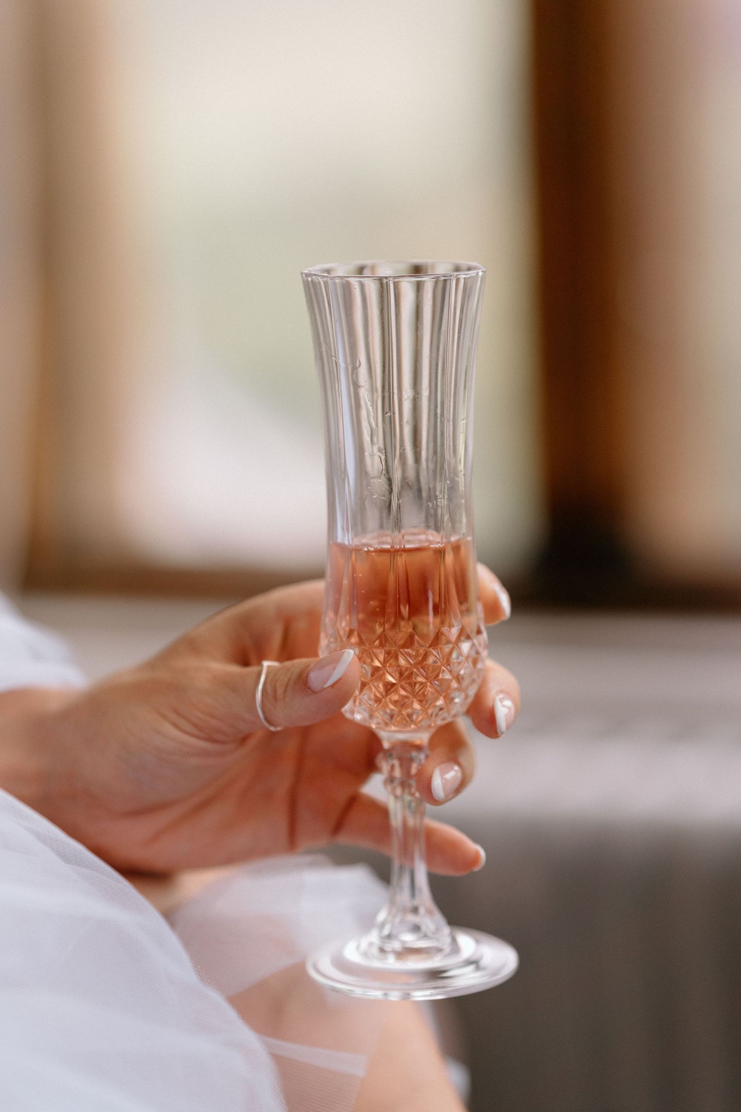 An elegant crystal champagne flute filled with rose-coloured champagne held by a manicured hand at Harlaxton Manor.