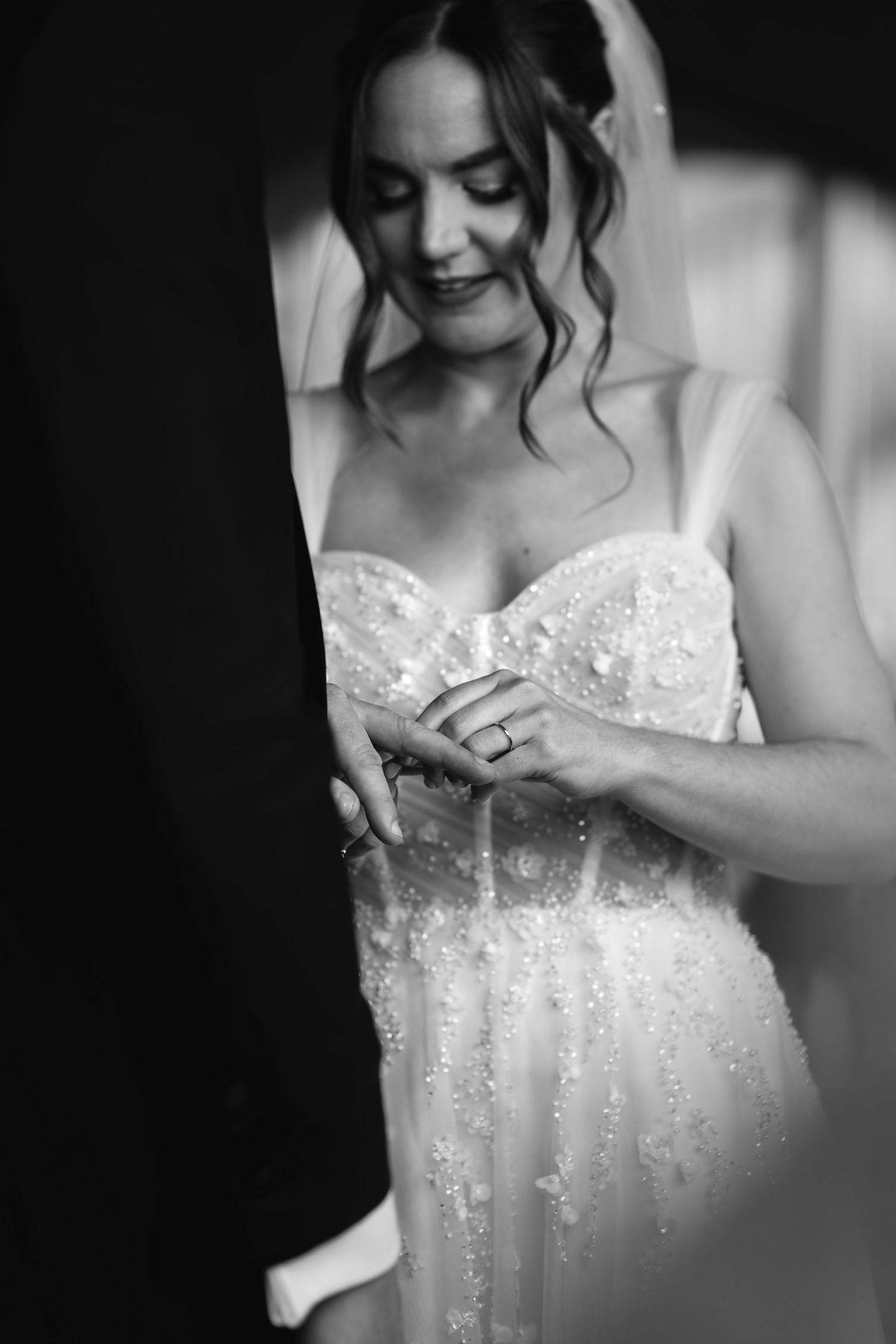 Bride in beaded strapless gown and veil looks down at her ring during wedding ceremony.