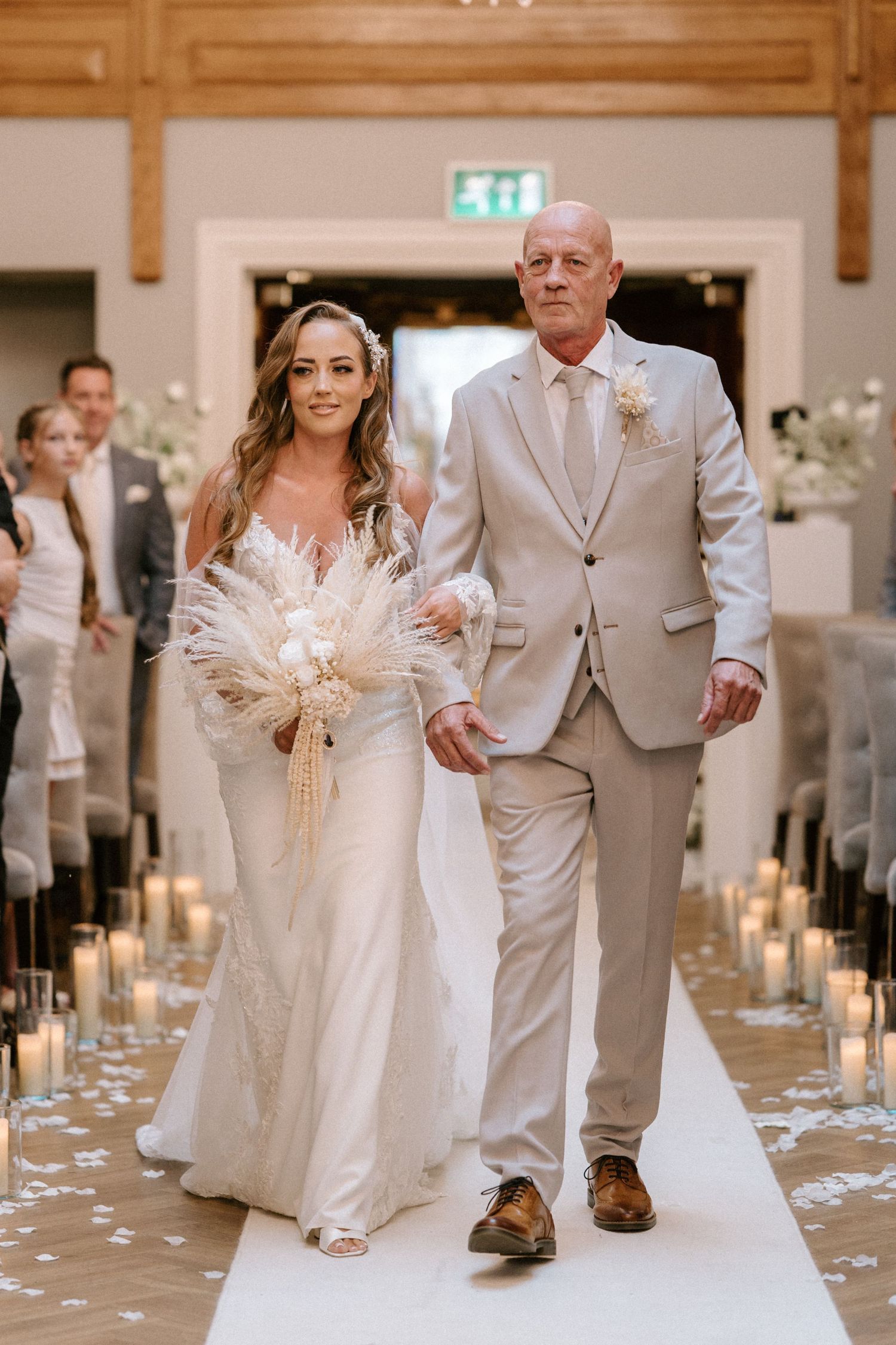 Wedding processional down a candle-lined aisle with natural decor and white floral arrangements.