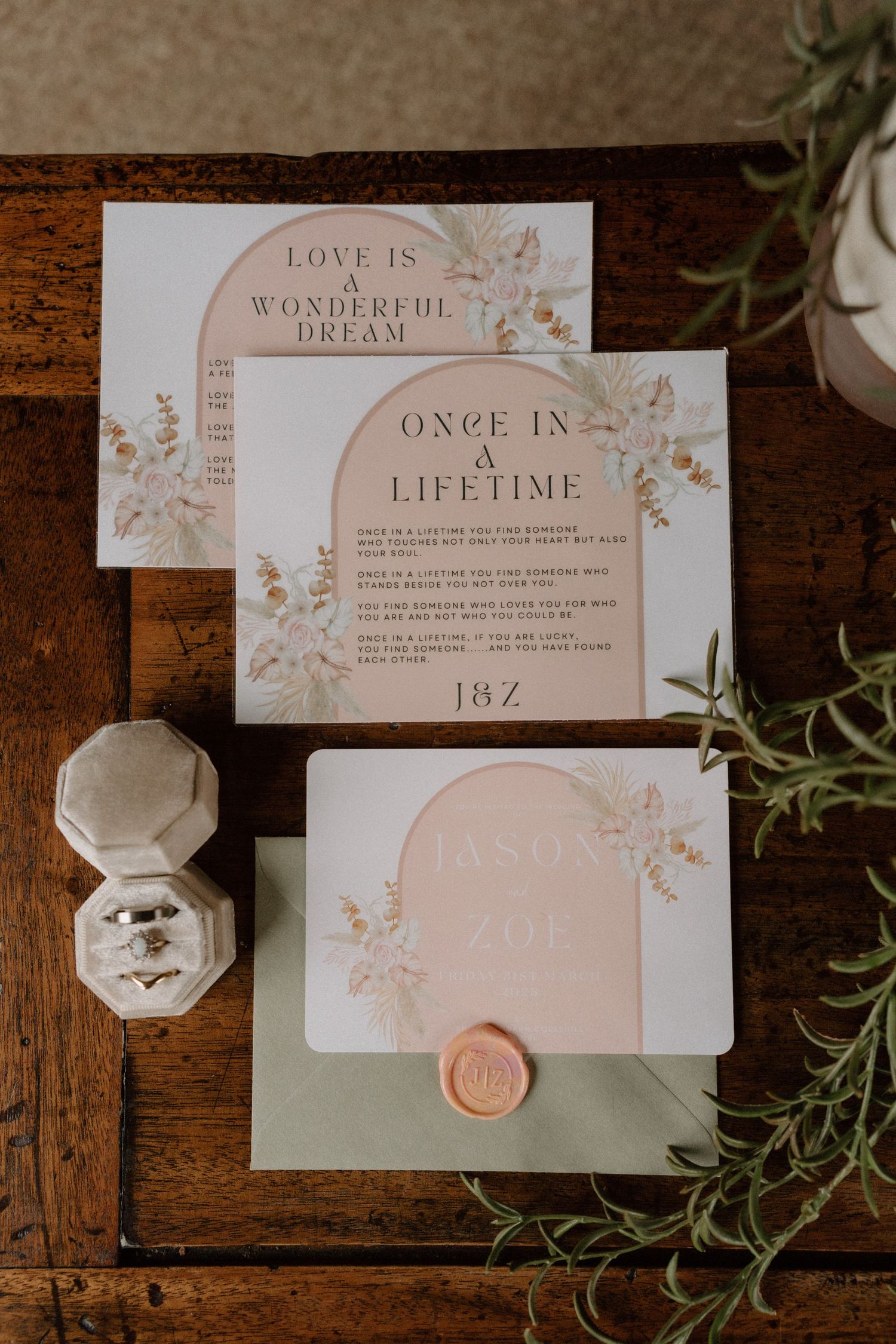 Elegant wedding invitation suite in blush pink and white with floral designs and a wax seal.