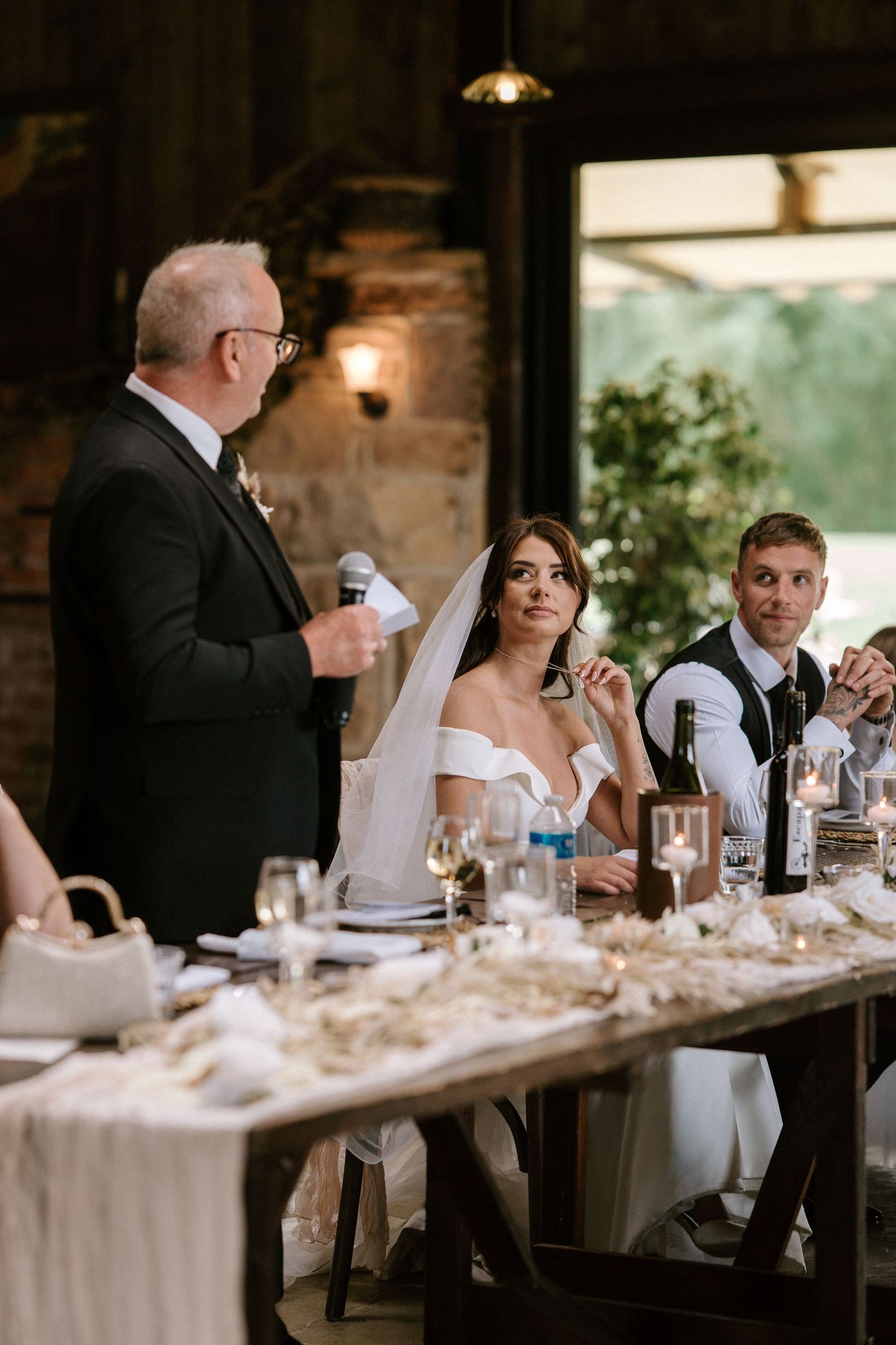 Wedding reception dinner scene with elegant table settings and glowing candlelight in rustic venue.