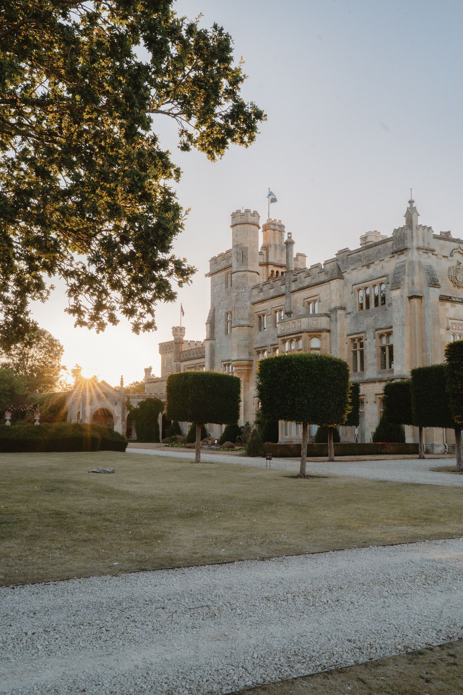 Golden sunset light illuminates a grand historic castle wedding venue surrounded by manicured gardens.