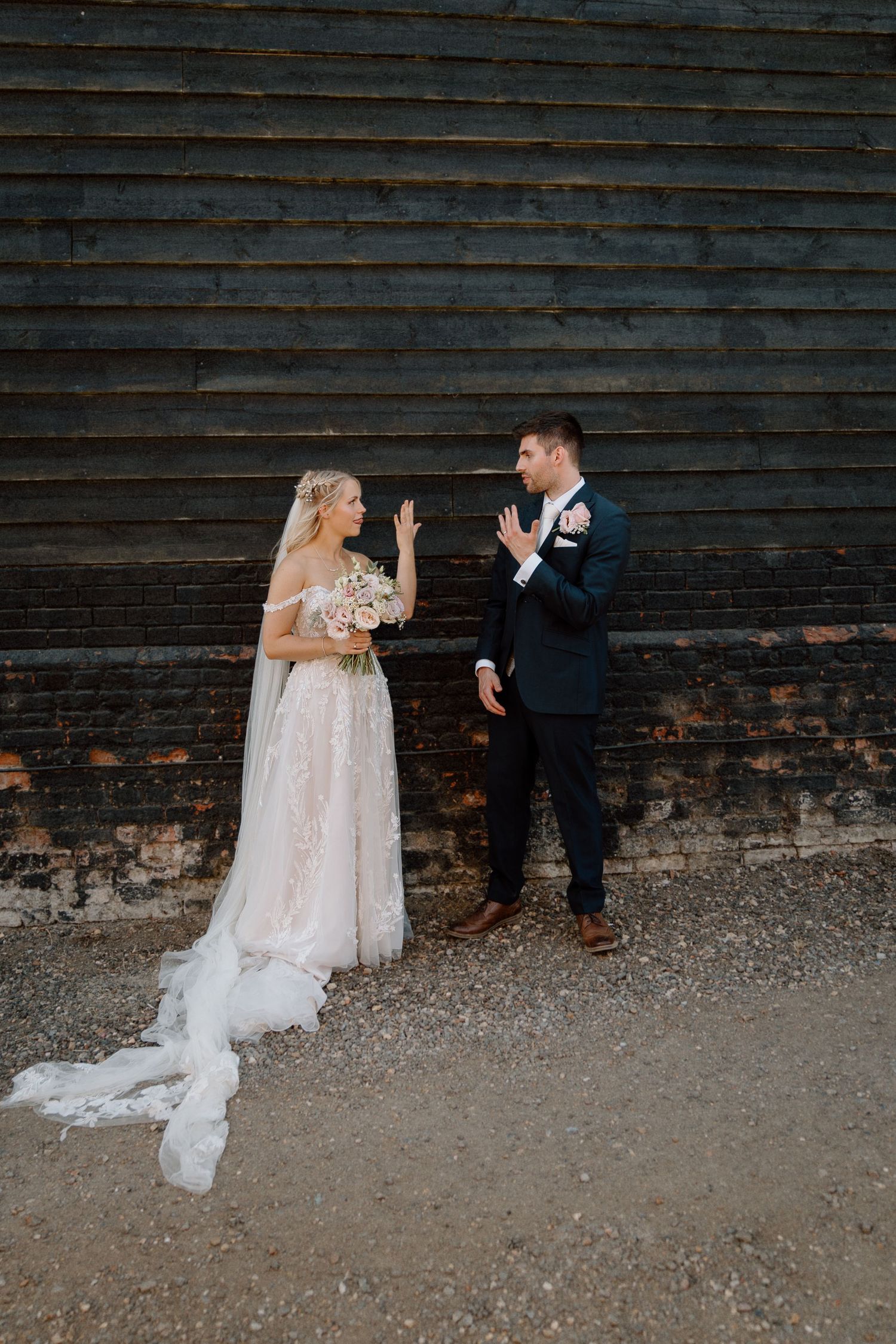 A couple shares a playful moment on their wedding day against a rustic wooden wall backdrop at Milling Barn.