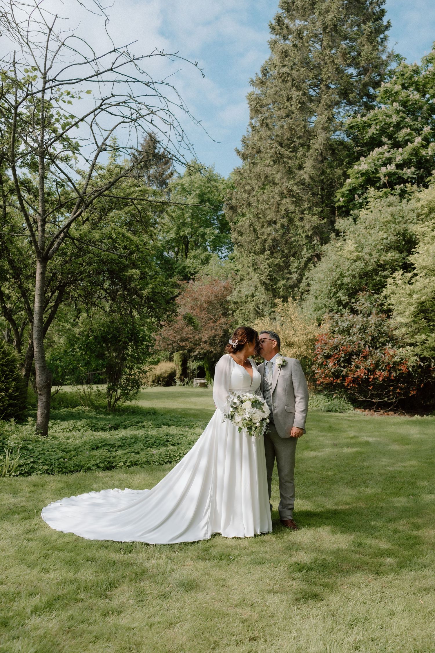 Couple shares intimate moment on manicured lawn with trees in background at Nuthurst Grange.