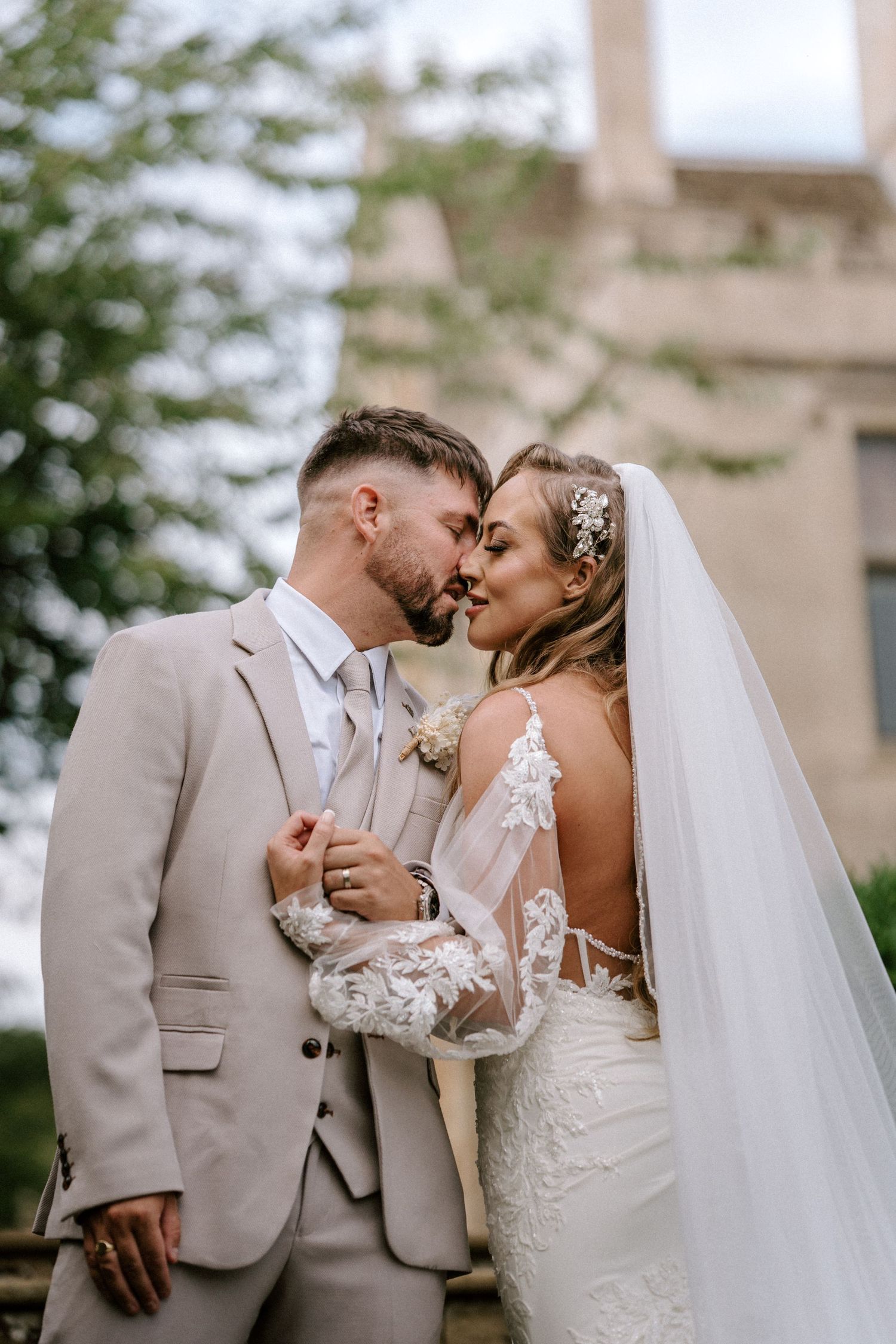 Romantic outdoor wedding portrait with light beige suit and lace gown.