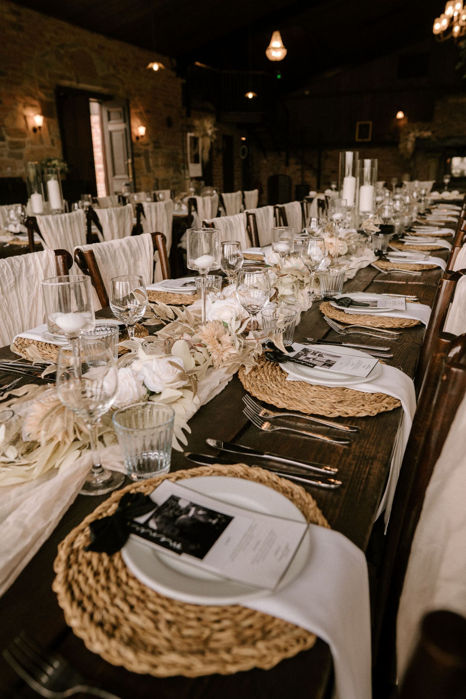 Elegant wedding reception table with woven chargers, crystal glasses and romantic lighting in stone venue.