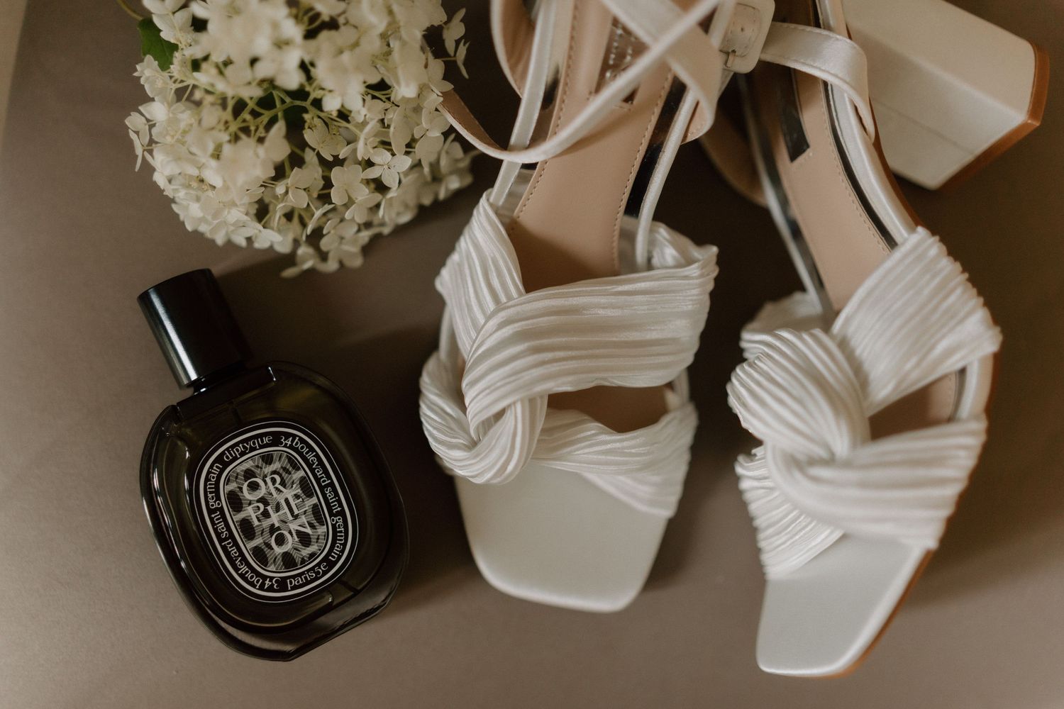 White strappy bridal shoes paired with a black perfume bottle on neutral surface at Dodford Manor.