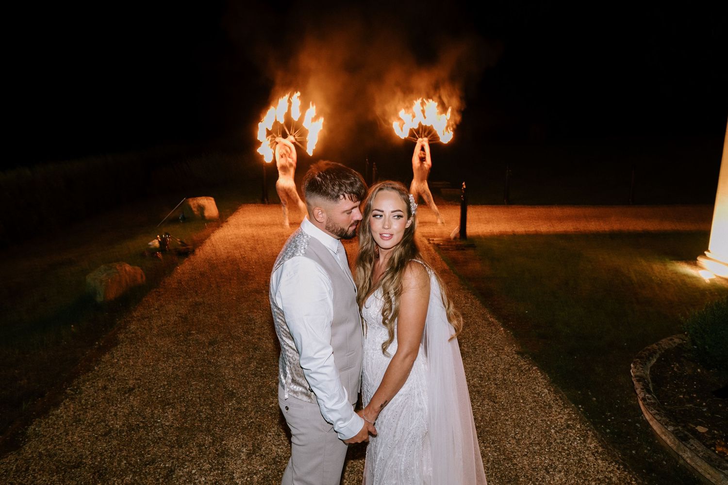 A couple poses with flaming sparklers creating a dramatic nighttime wedding photo.