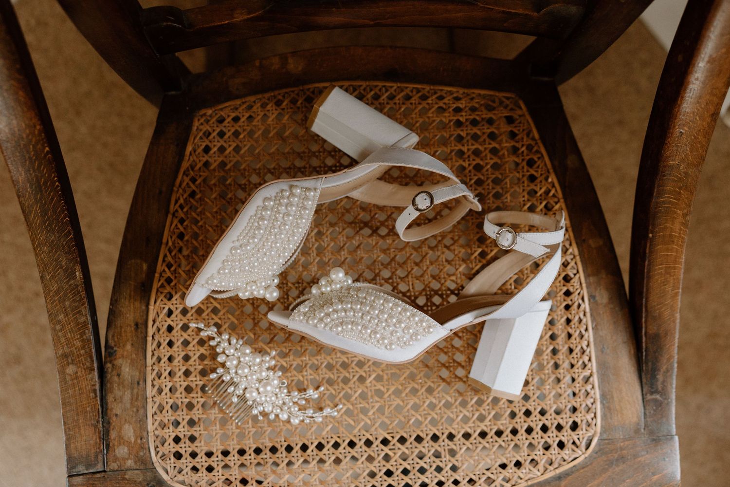 White bridal shoes with lace details placed on a woven rattan chair.
