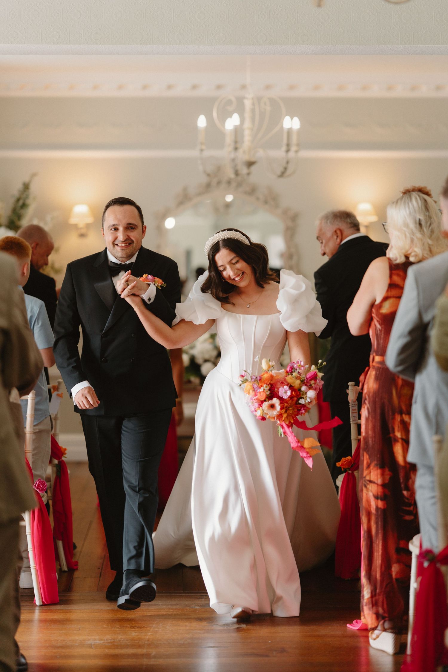 Joyful bride and groom walking down the aisle, bride holding vibrant pink and orange bouquet.