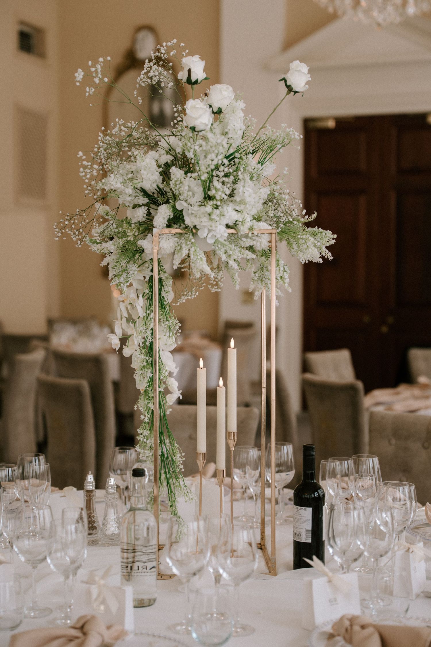 White floral centerpieces with tall glass vases and candles decorate an elegant wedding reception table.
