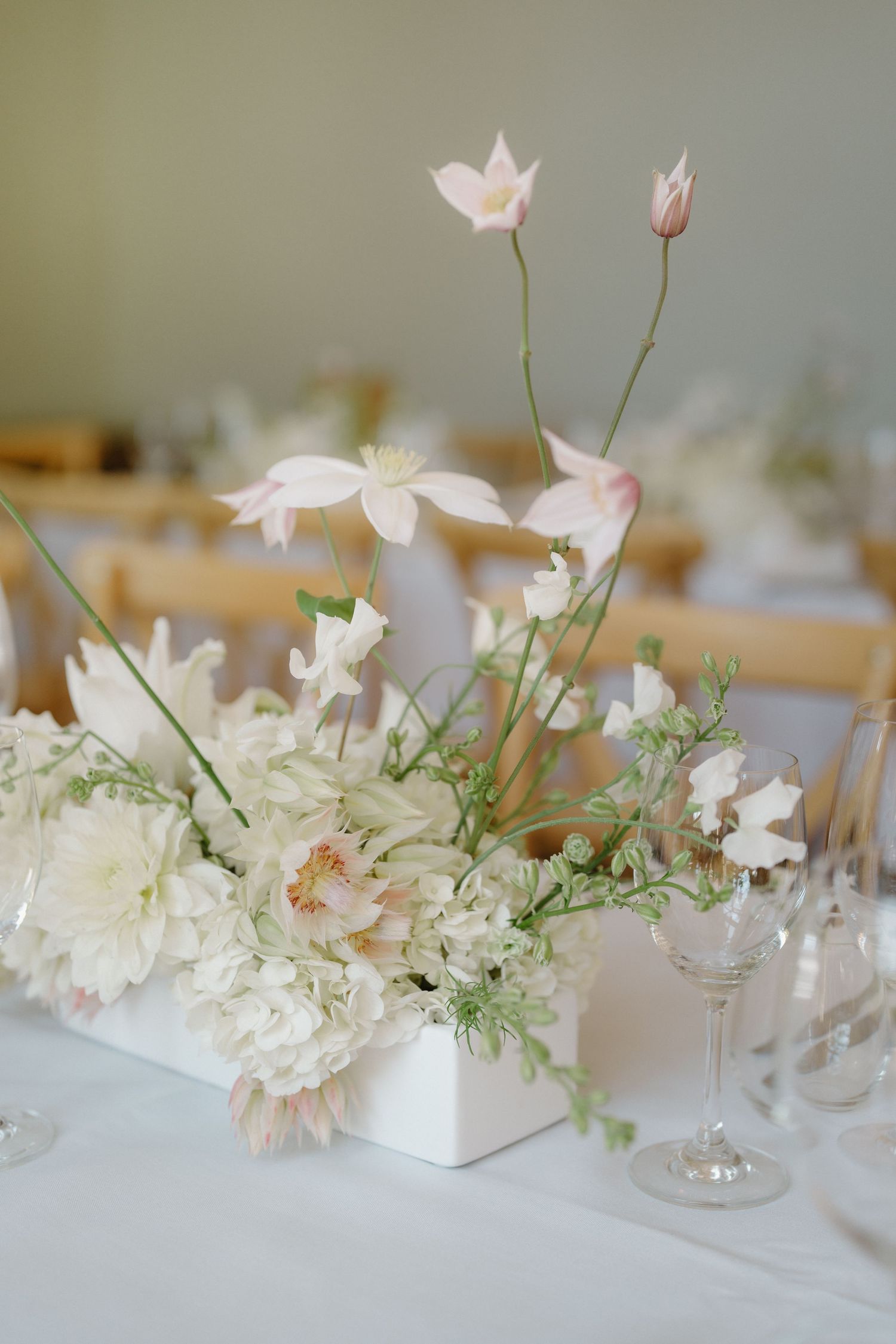Elegant wedding table centerpiece with white and blush pink flowers including dahlias and cosmos in a white vase.