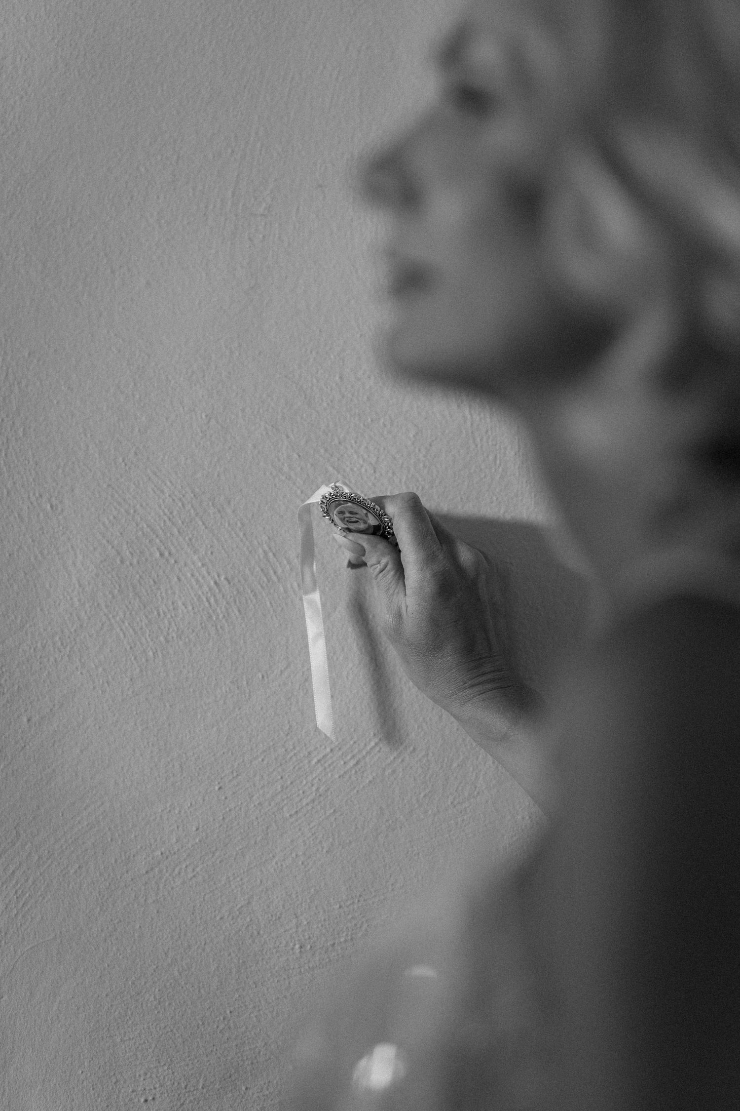 Black and white close-up of a blonde bride holding a delicate floral ring, with soft bokeh background.