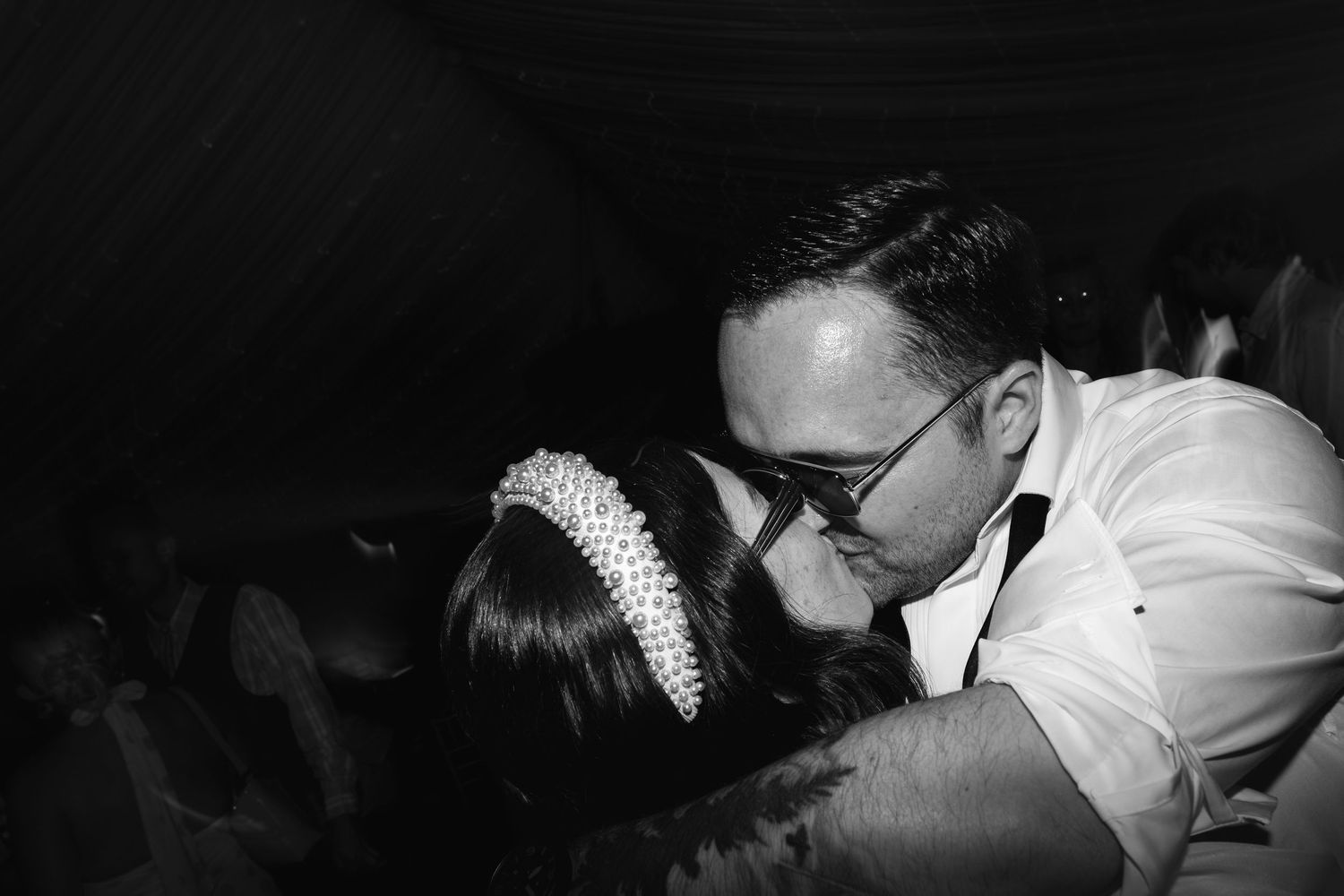 Black and white photo of a couple sharing a romantic kiss at a formal event, woman wearing a pearl headband.