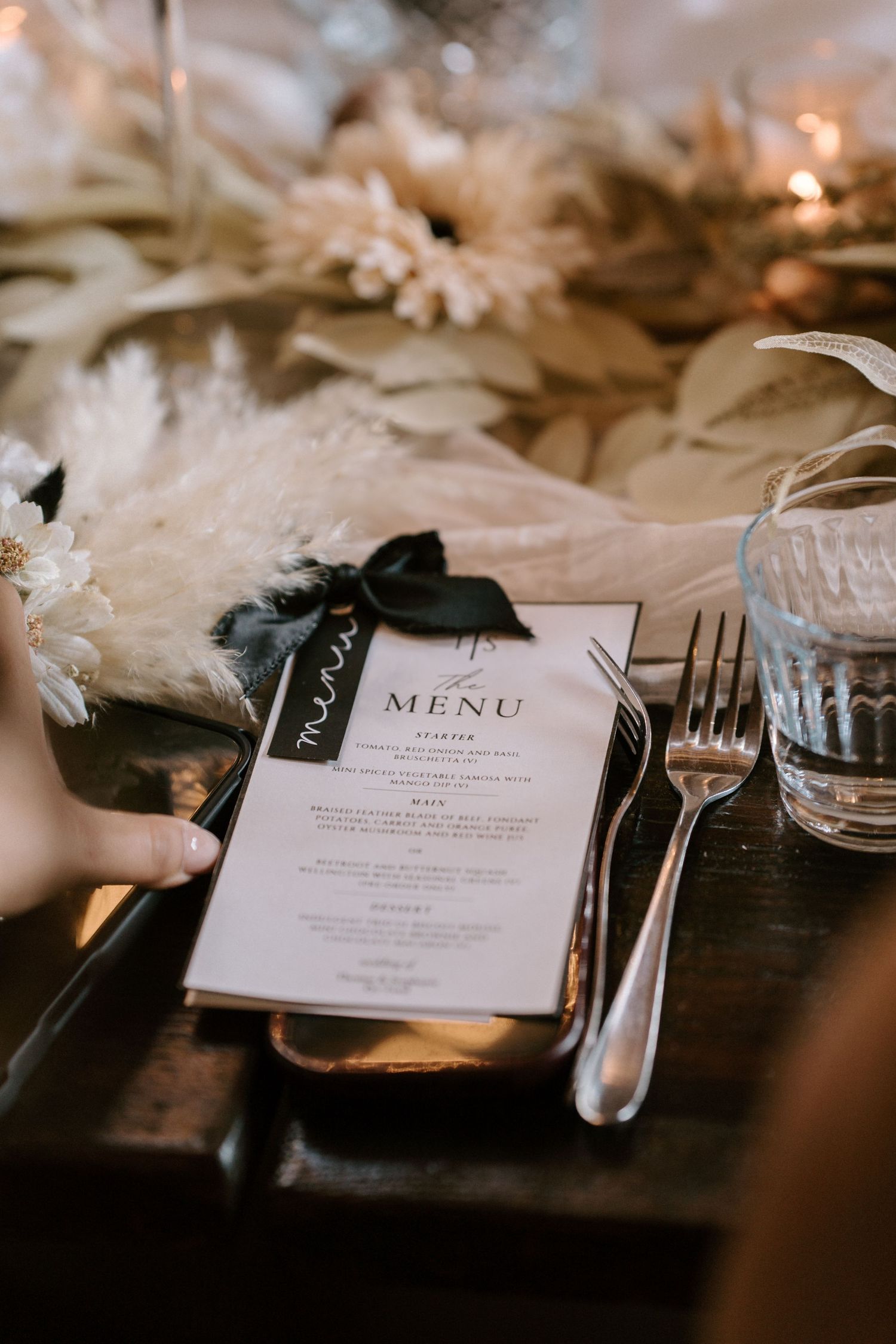Wedding menu card and place setting on a wooden table with elegant dinnerware and soft lighting.