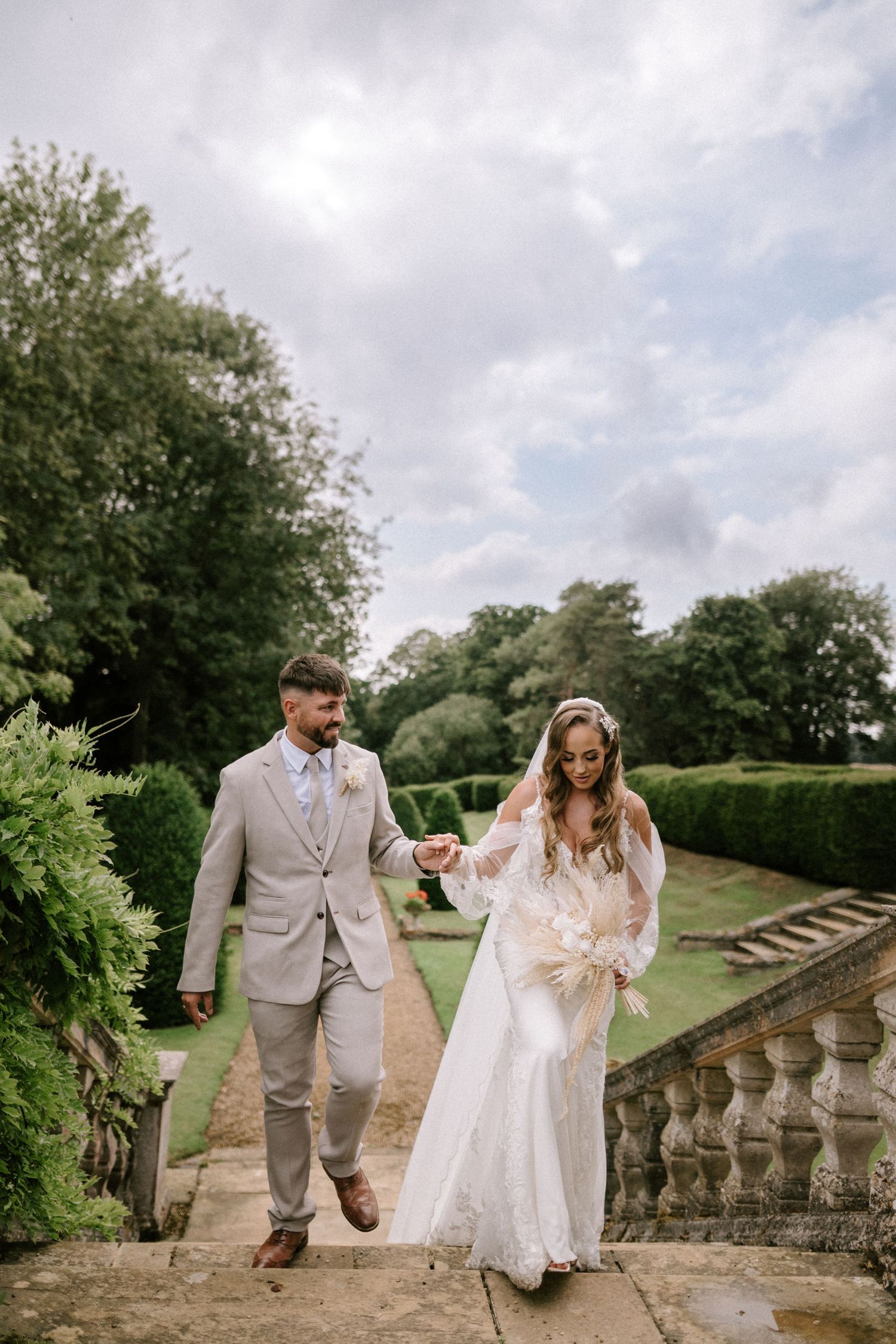 Couple walks along scenic garden balustrade path during wedding photoshoot.
