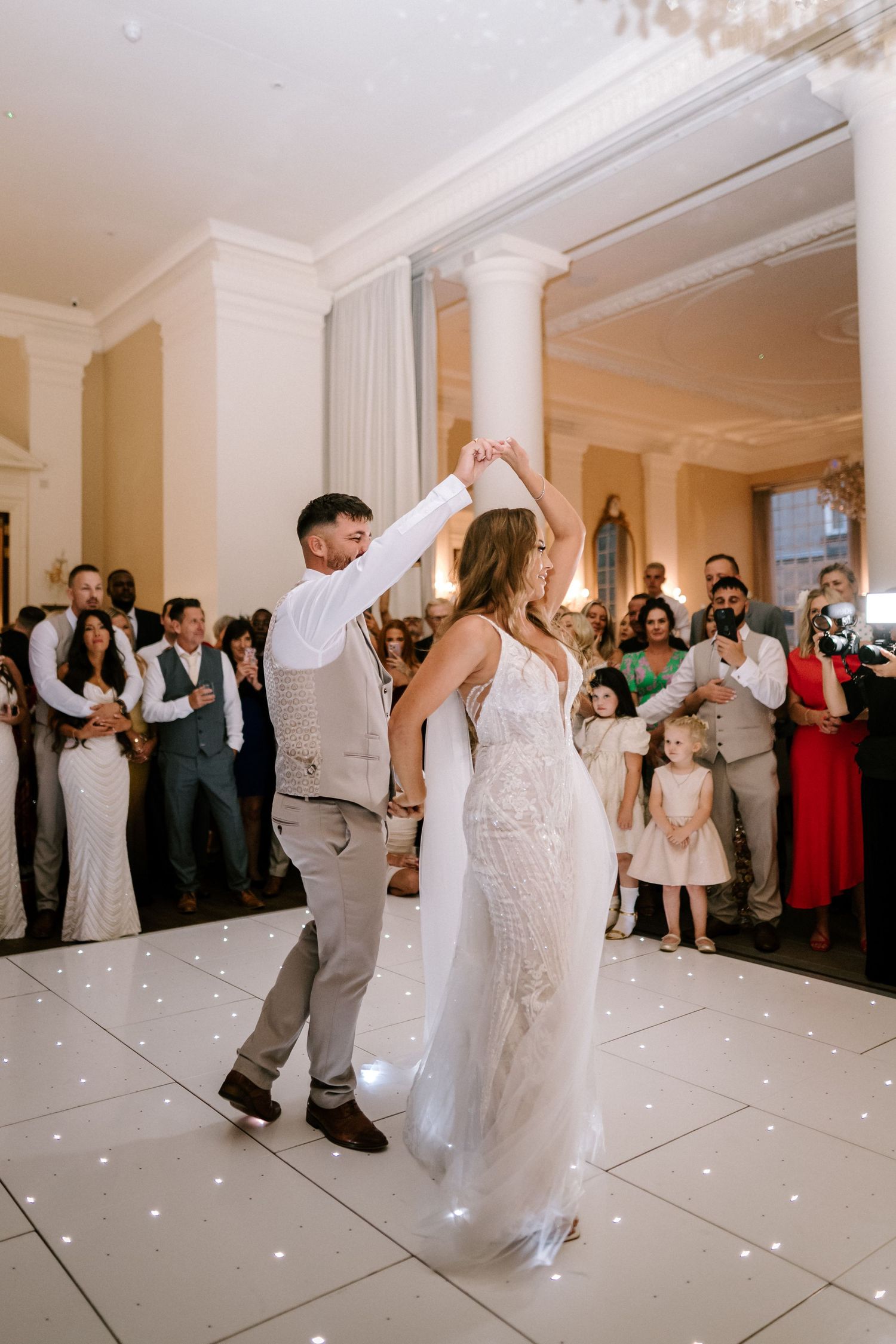Couple performs first dance on illuminated white dance floor at wedding reception.