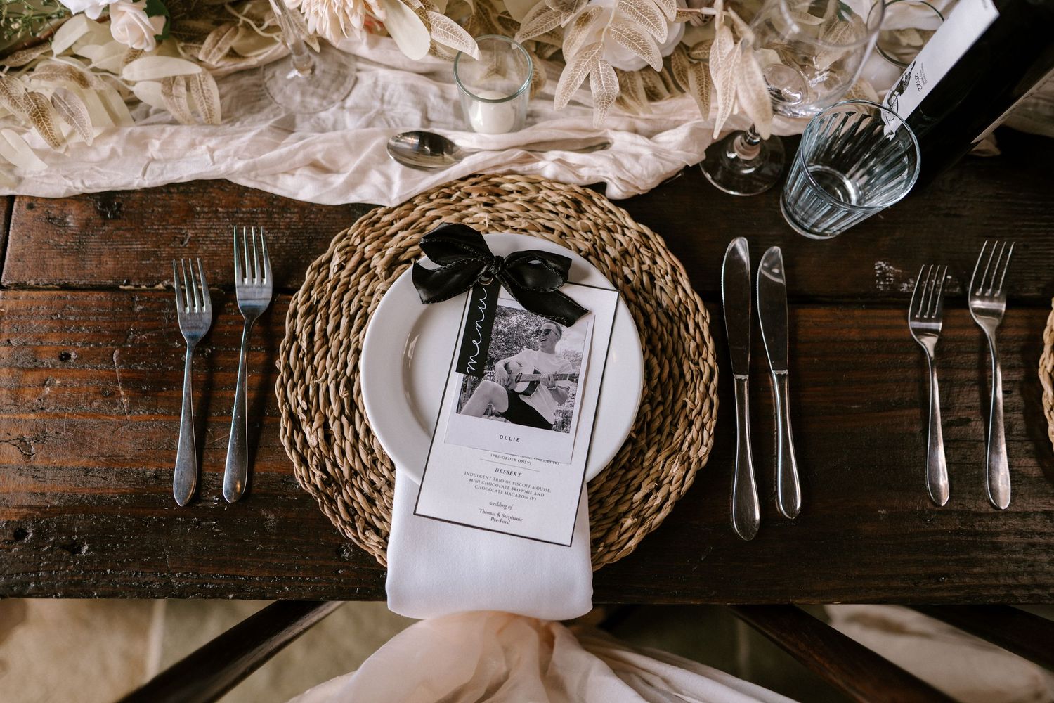 Overhead view of rustic wedding place setting with woven charger, silverware and photo card.