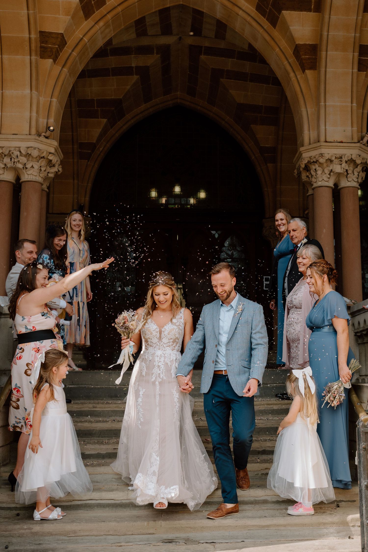Wedding party celebrates on church steps as flower girls throw confetti during the ceremony exit in Northampton.
