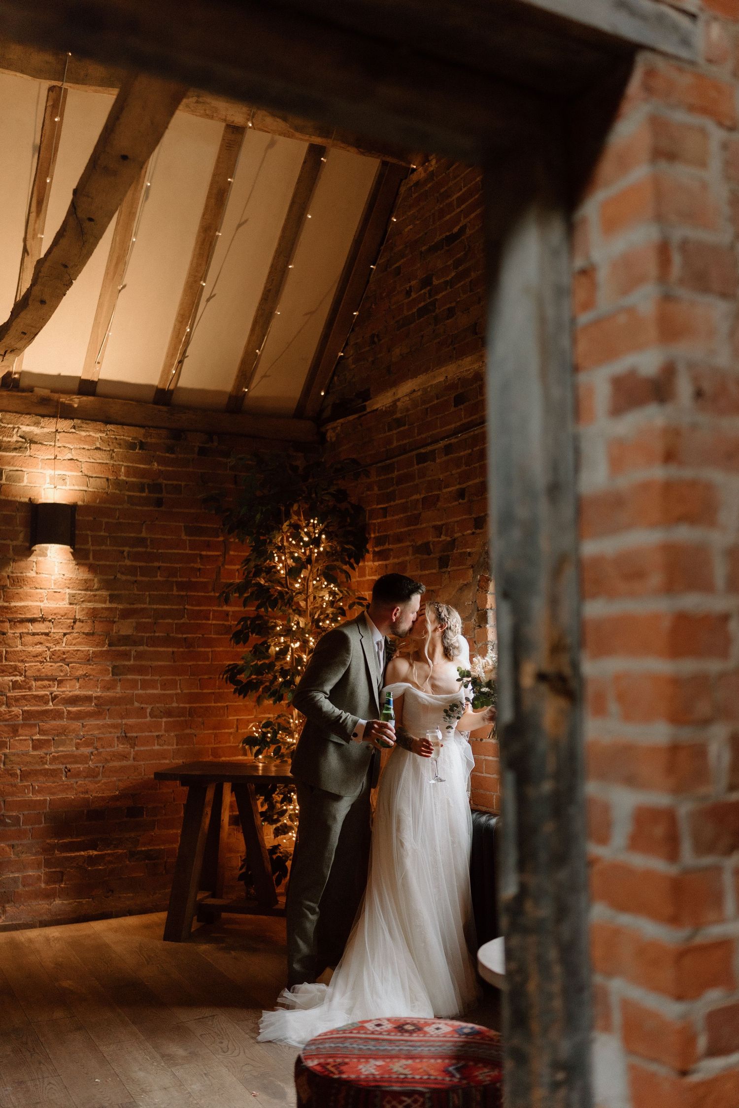 Romantic wedding moment captured in a rustic brick venue with warm lighting and wooden beams at Shustoke Barn.