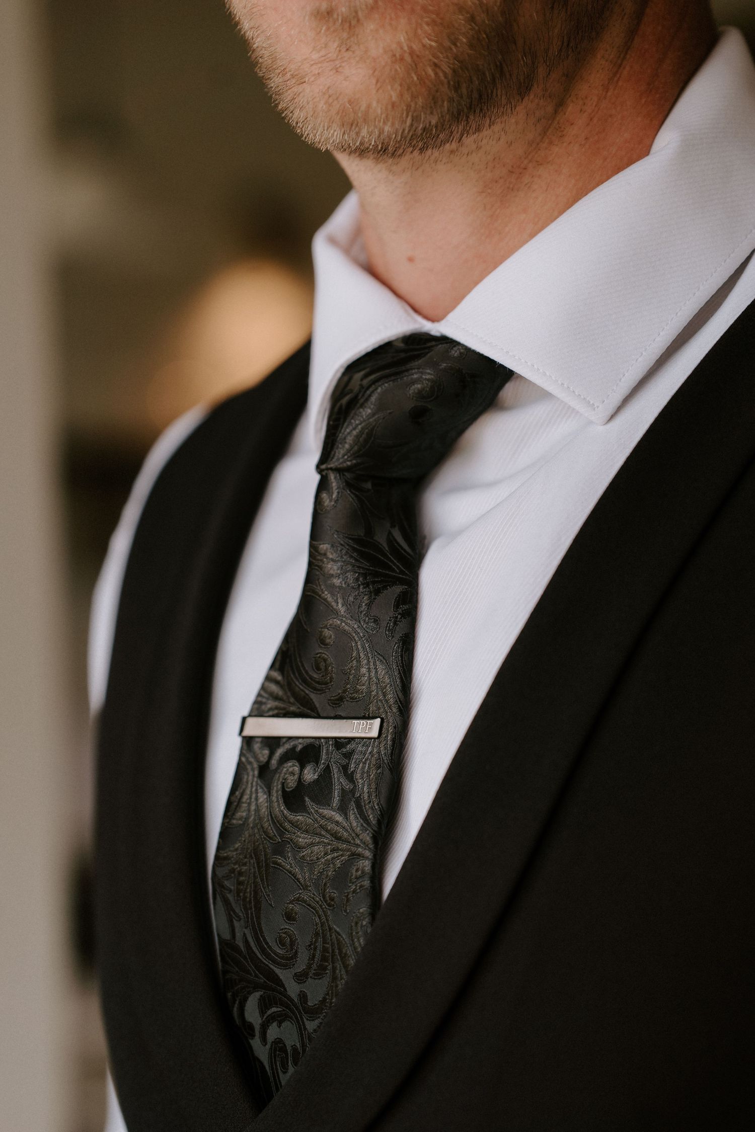 Close-up detail shots of a black formal tie with textured paisley pattern against crisp white dress shirt and dark suit.